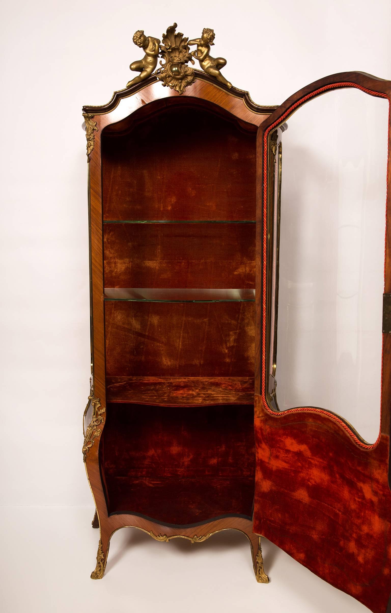 A beautiful quality rosewood vitrine or display cabinet richly adorned with ormolu mounts and three painted panels in the Vernis Martin manner, 19th century. The interior is lined with red velvet and has two glass shelves. The top is crowned with