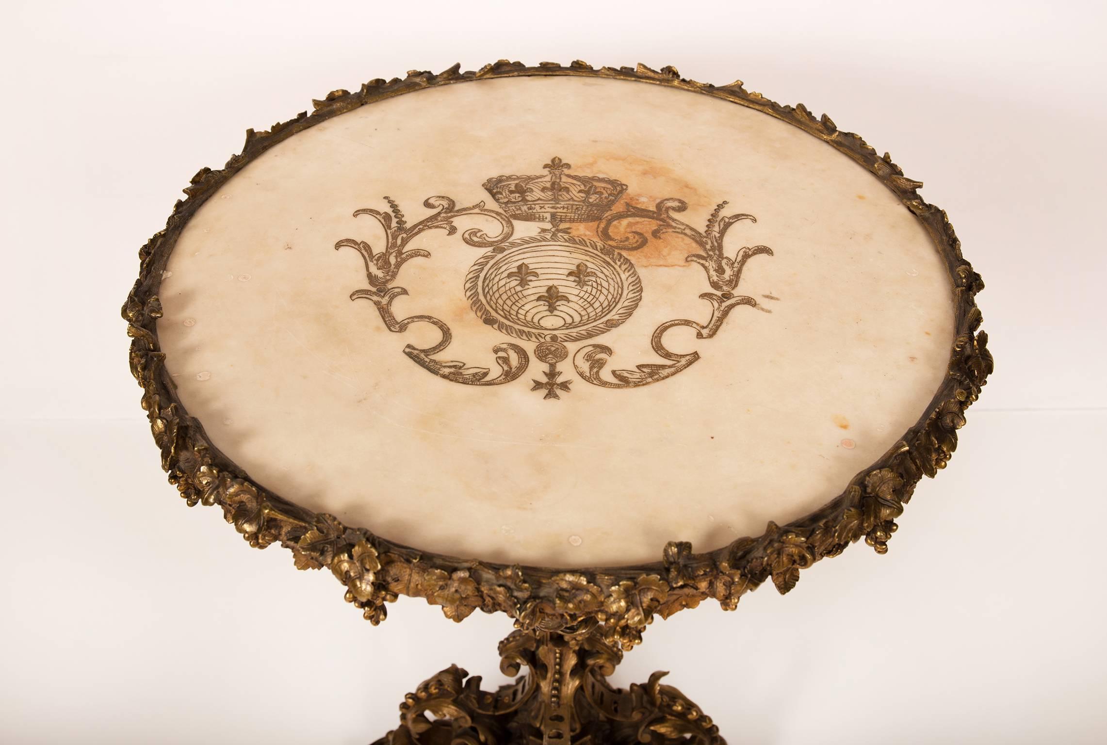 Lovely and rare bronze gueridon table with a white carrara marble top, carved with a polychromed crest of fleur de lys in a cartouche and a Knights Cross. The marble top set in a bronze mount of vineleaves and grapes; the baluster stem with four