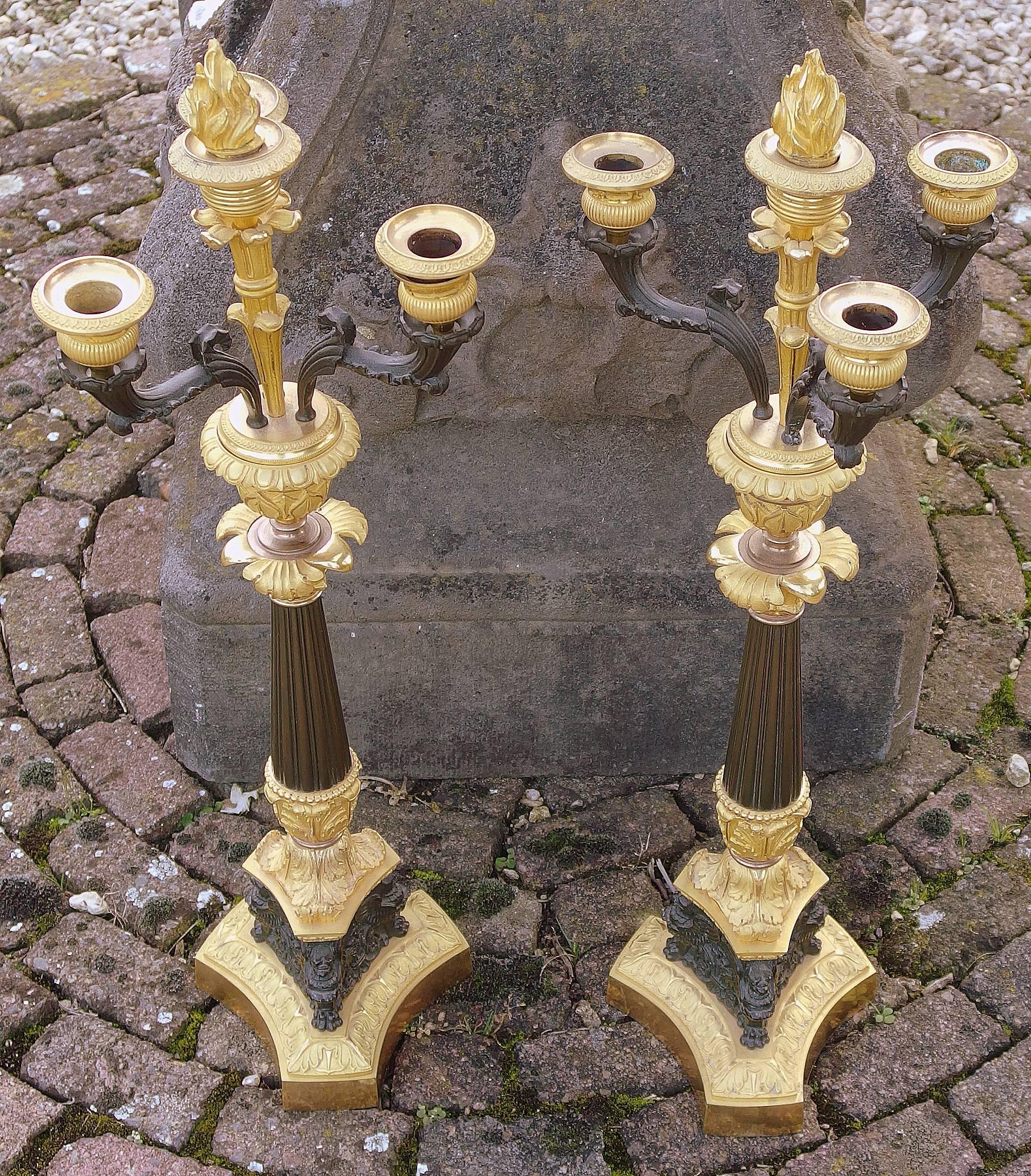 A pair of Ormolu and Patinated Bronze Candelabra in the Louis Philippe style, made in France around 1830. The candelabra each have four candleholders. On an octagonal base, each candelabra has a removable flame cap in the socket of the upper