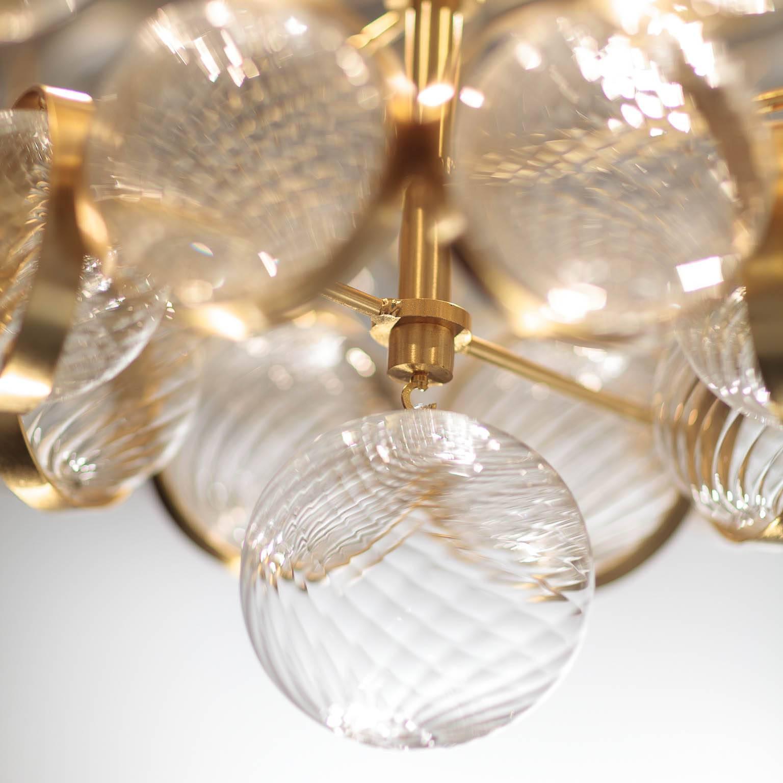 With satin gold metal and handblown clear glass spheres with spiral ribbing, the Atomos is symmetrically aligned but also has a rich vitality and brightness to it. Each textured glass ball within this lively cluster is held within a flat metal ring