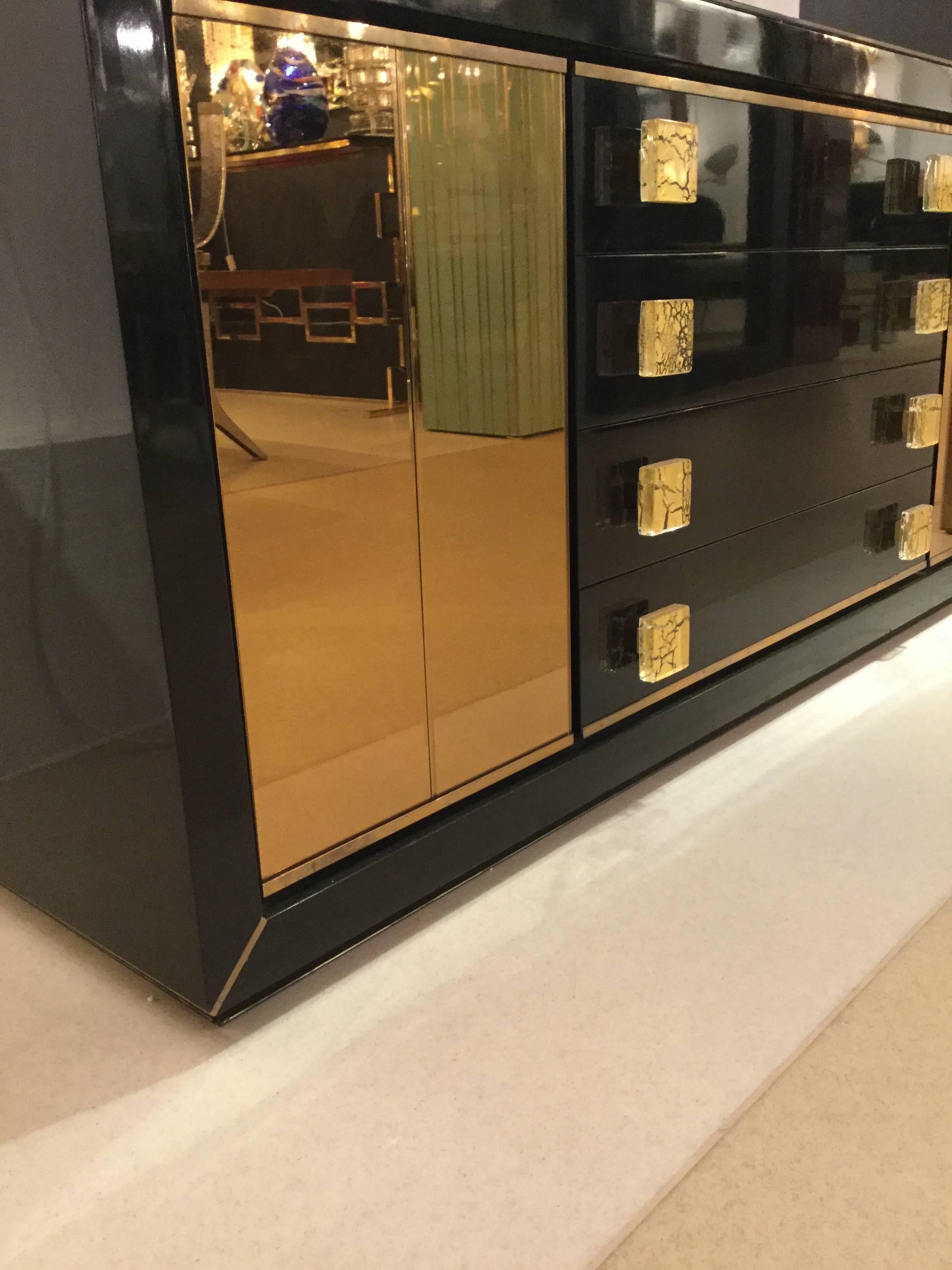 A 1960s Italian designed sideboard, black lacquer with brass profiling, two glass door panels and four drawers with Murano glass door handles.