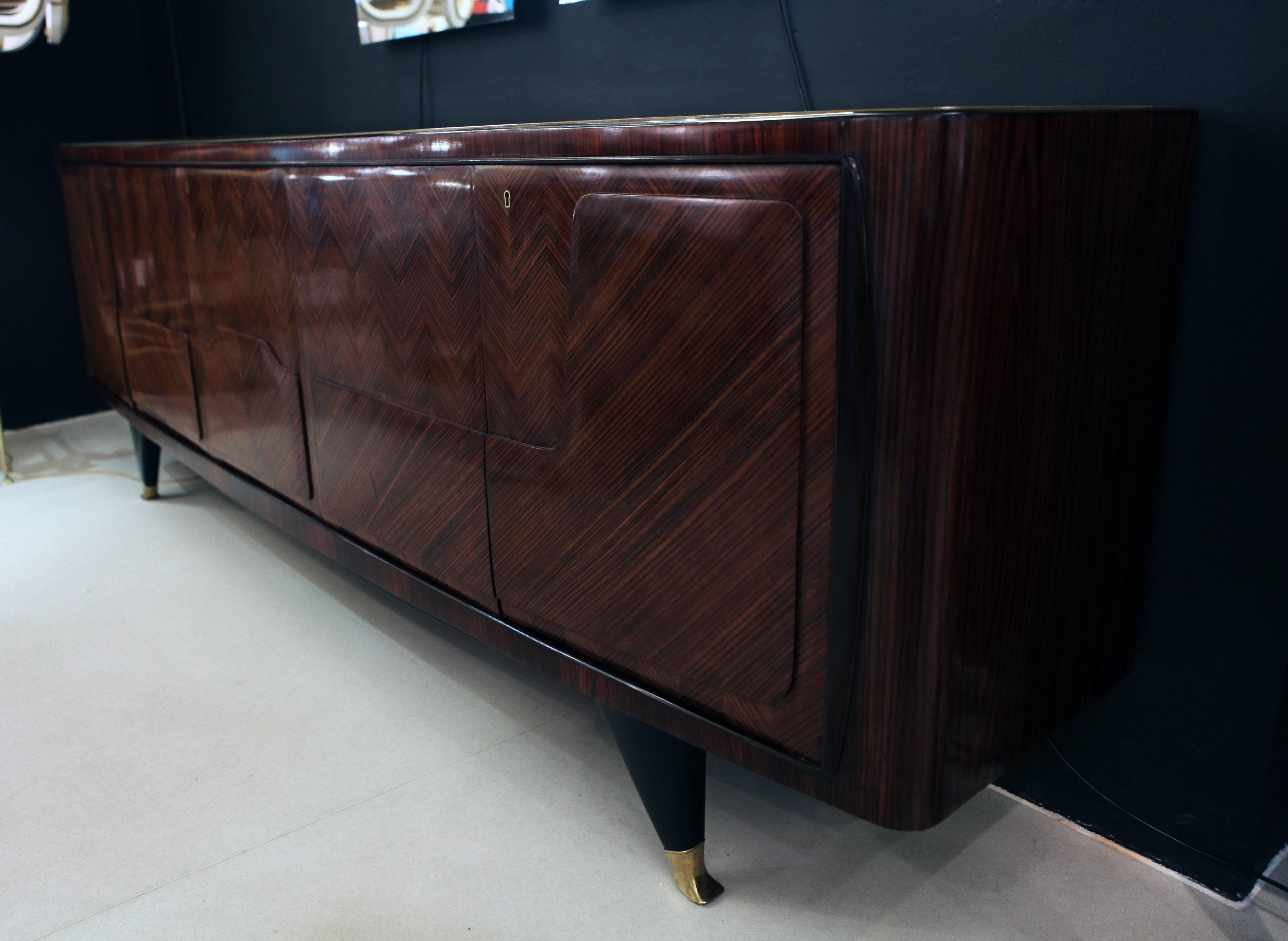 An elegant sideboard with a beautiful walnut marquetry , ebonized legs on brass feet and golden venetian glass top. On the two sides has cupboards with wooden shelves and in the middle door there are five hidden drawers.
In excellent vintage