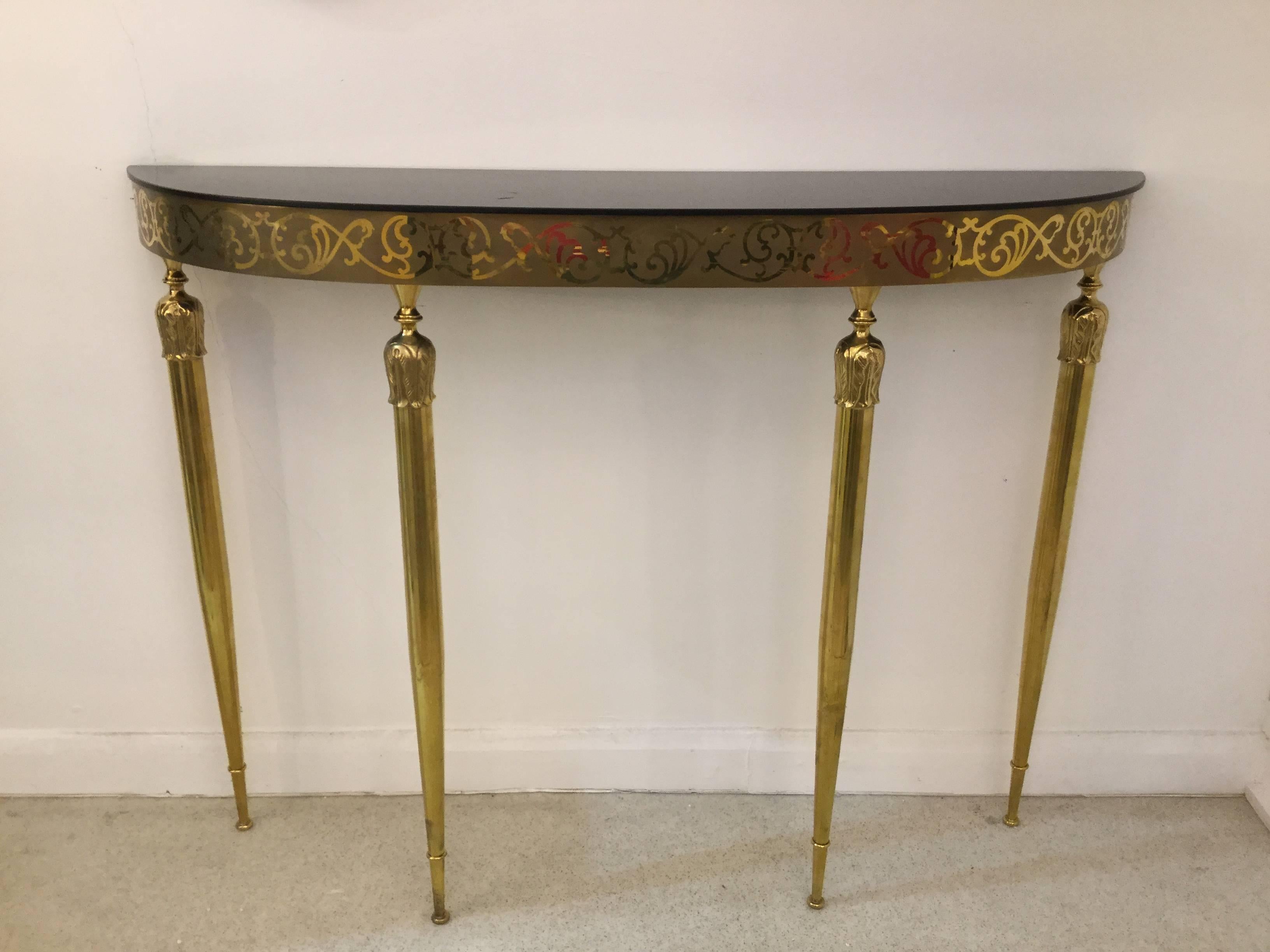 A demilune console table in brass with decorated motifs and black glass top.