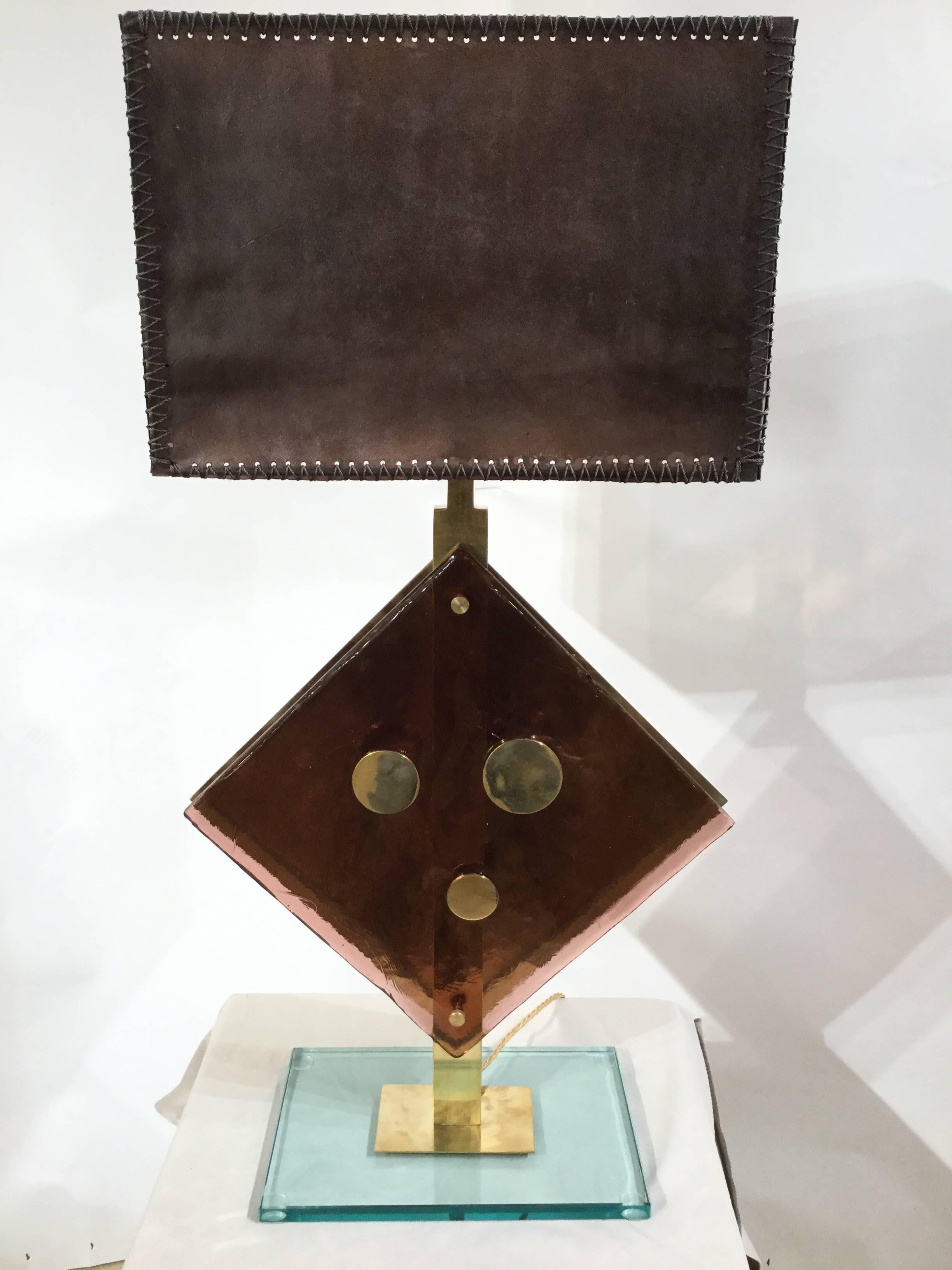 This stunning pair of table lamps consists in a square brown Murano glass central piece decorated with three brass circle of different size. The frame, in brass, is mounted on a glass base.
 