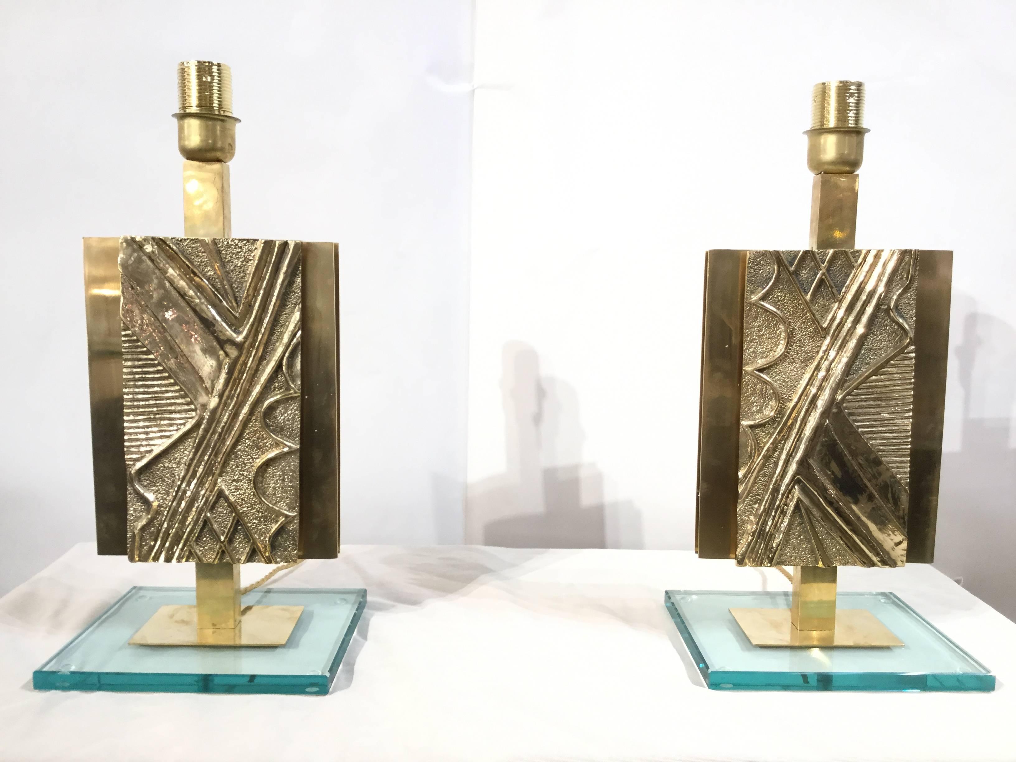 A pair of tall table lamps made of a rectangular glass base, brass structure and cast bronze facades.