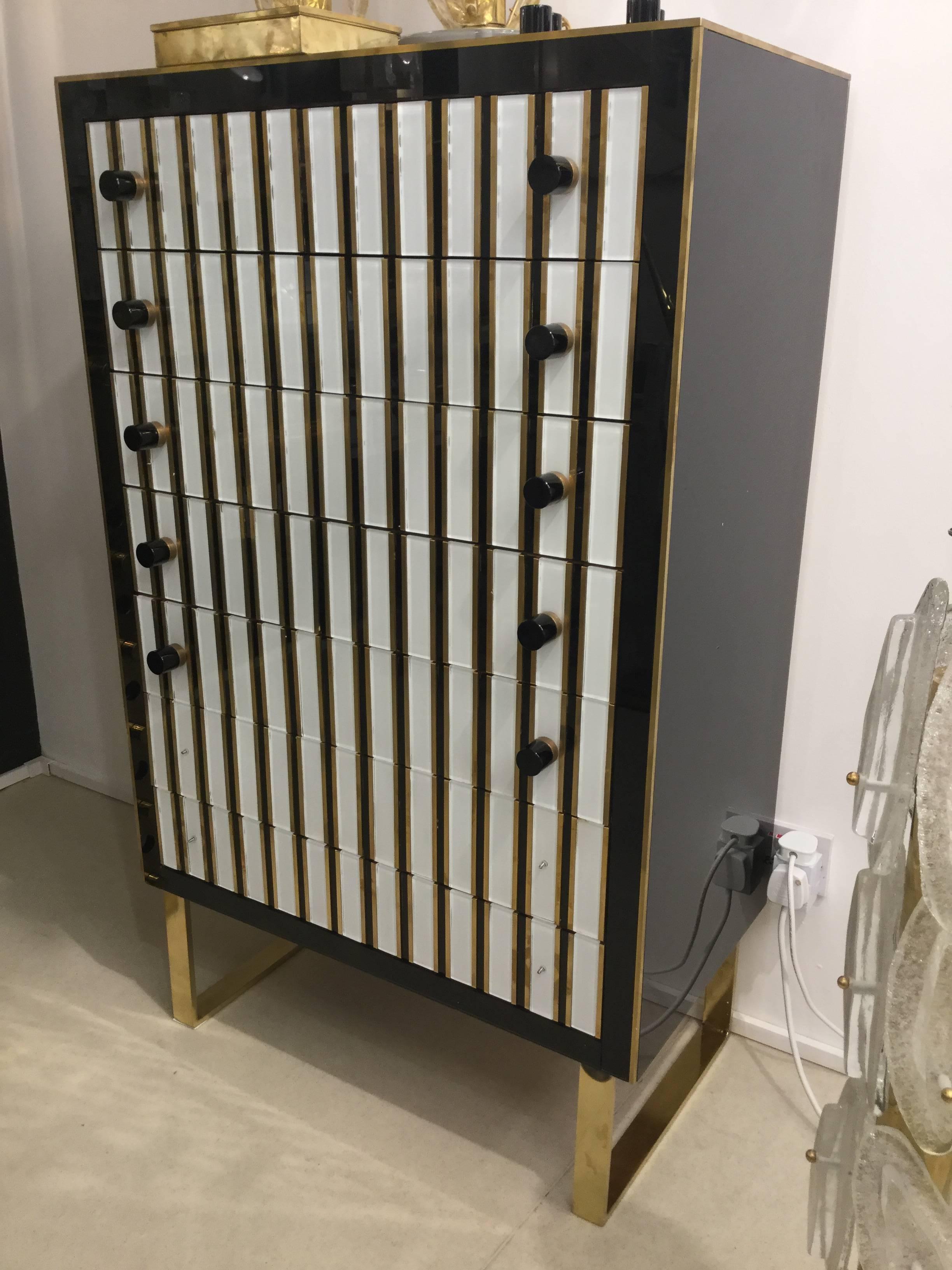 An Italian designed Postmodern Venetian 7 day chest of drawers in black and white glass inlaid with brass Murano black glass handles on brass legs, circa 1980.