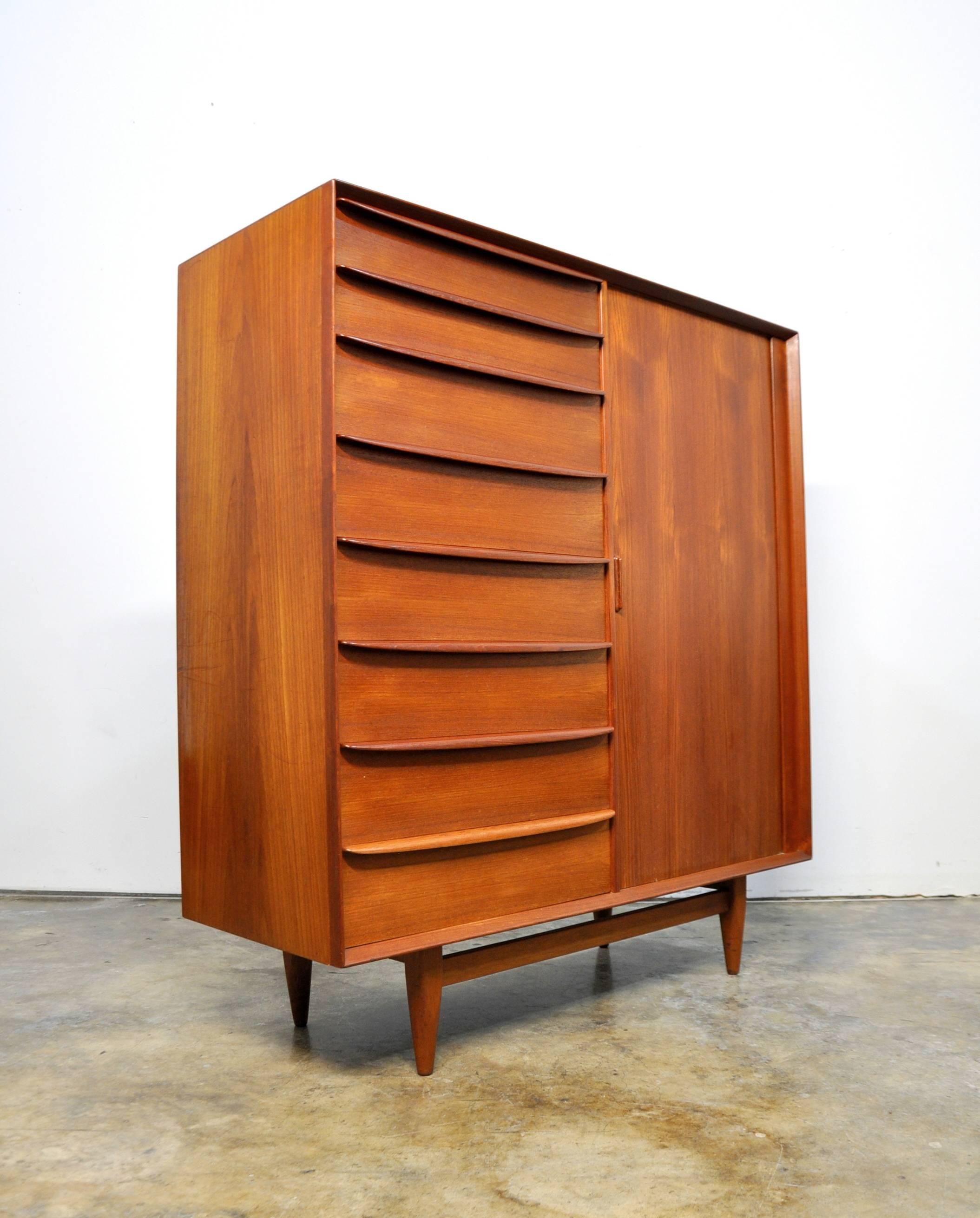 Both gorgeous and functional, this Mid-Century Danish modern bachelor's chest of drawers dates from the 1960s. With a total of 17 drawers, it provides a ton of storage space. The vintage wardrobe features sculpted teak handles, tambour door and