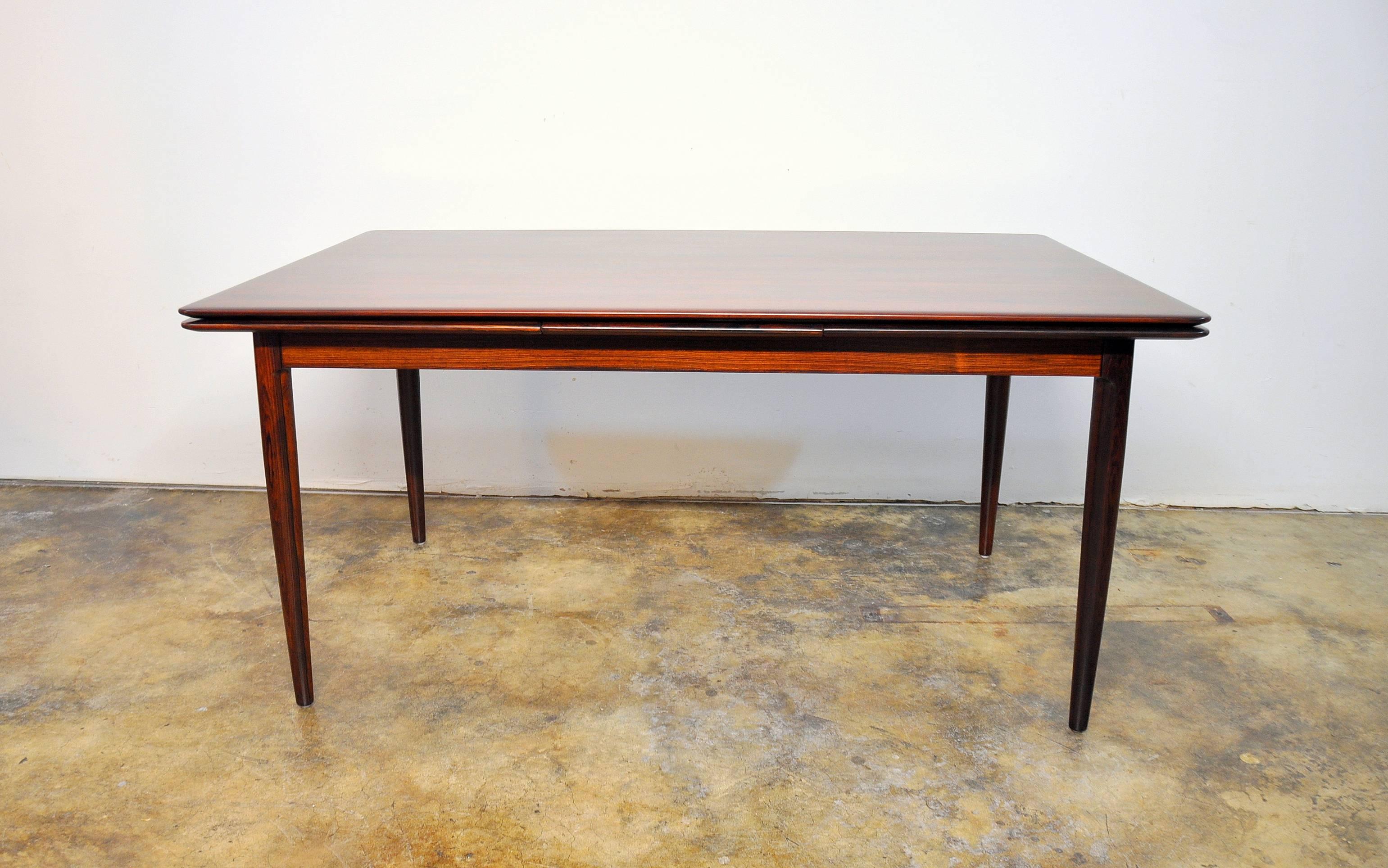Amazing Mid-Century Danish modern rosewood expandable dining table, dating from the 1960s. The table has a draw leaf design and can extend to 104". It has two leaf extensions that draw out from their original position tucked underneath the main