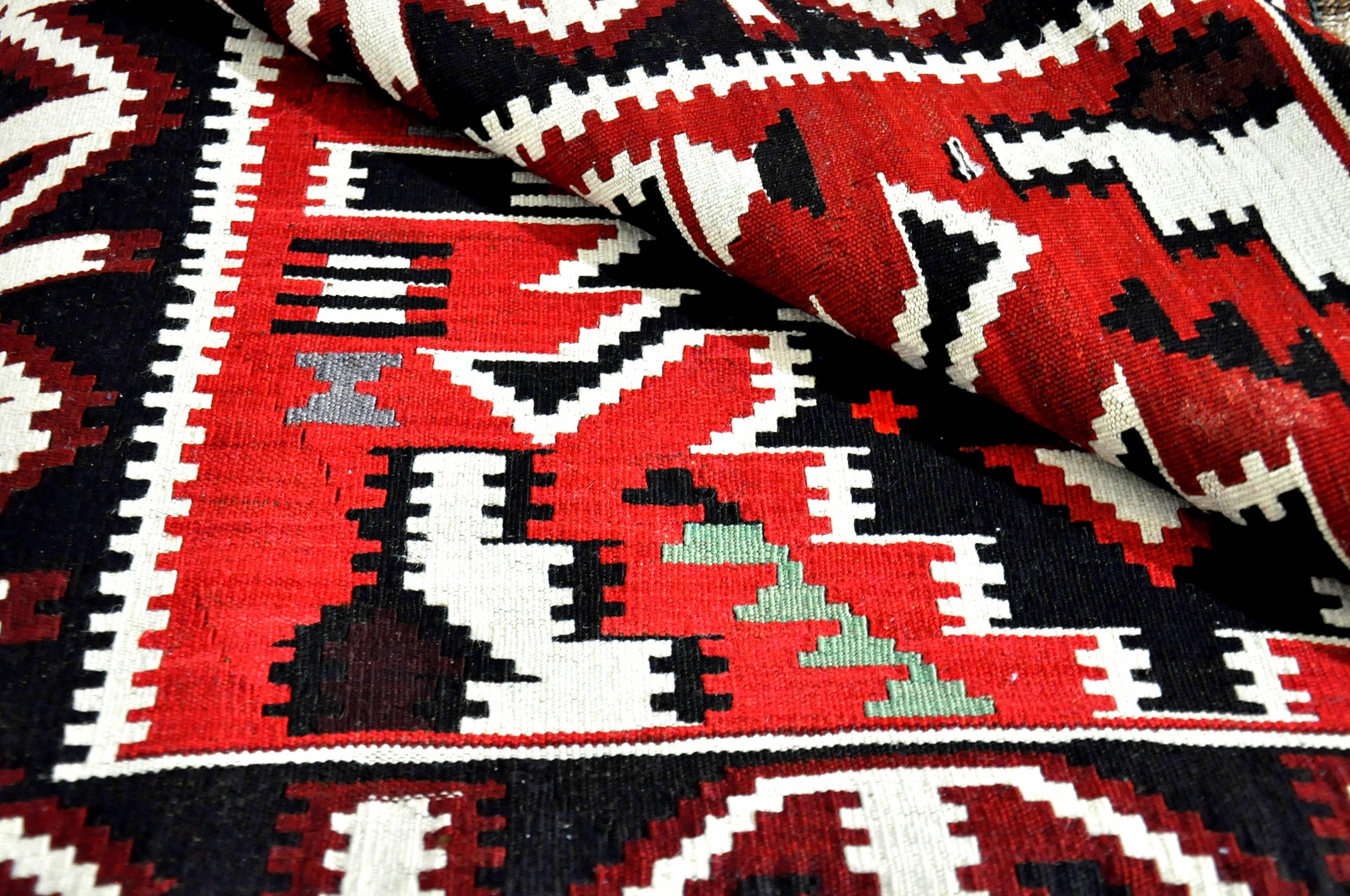 This Quba Kilim rug from the Daghestan region of Caucasus, not far from the Caspian Sea, features traditional vibrant tribal red and black elements, with contrasting gold and white spaces. Beautifully fringed ends meet tightly woven borders with