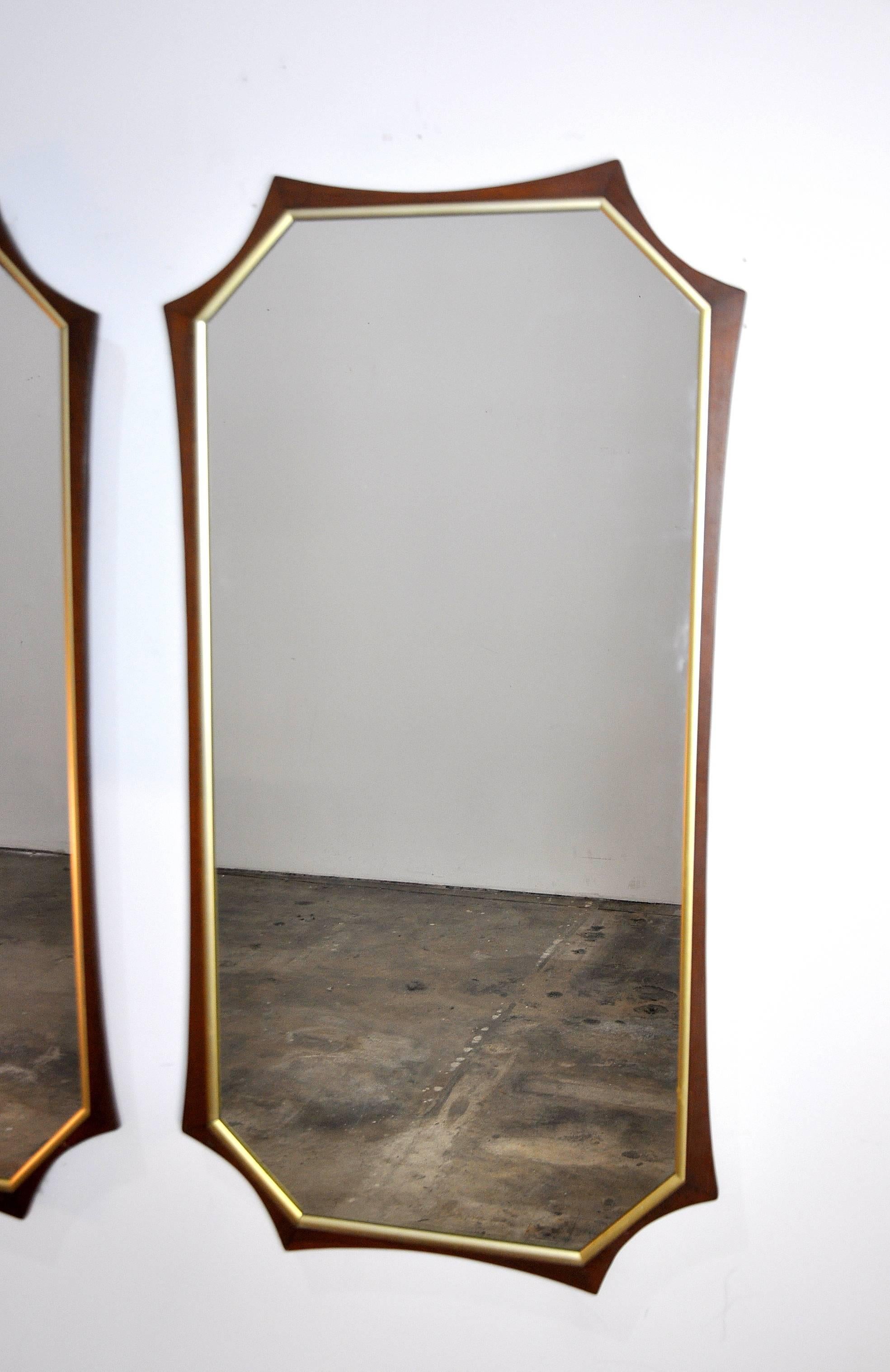 An eye-catching pair of vintage Mid-Century mirrors dating from the 1960s. Each large mirror features an octagonal walnut frame with brass toned trim. A unique find that will instantly decorate any room.