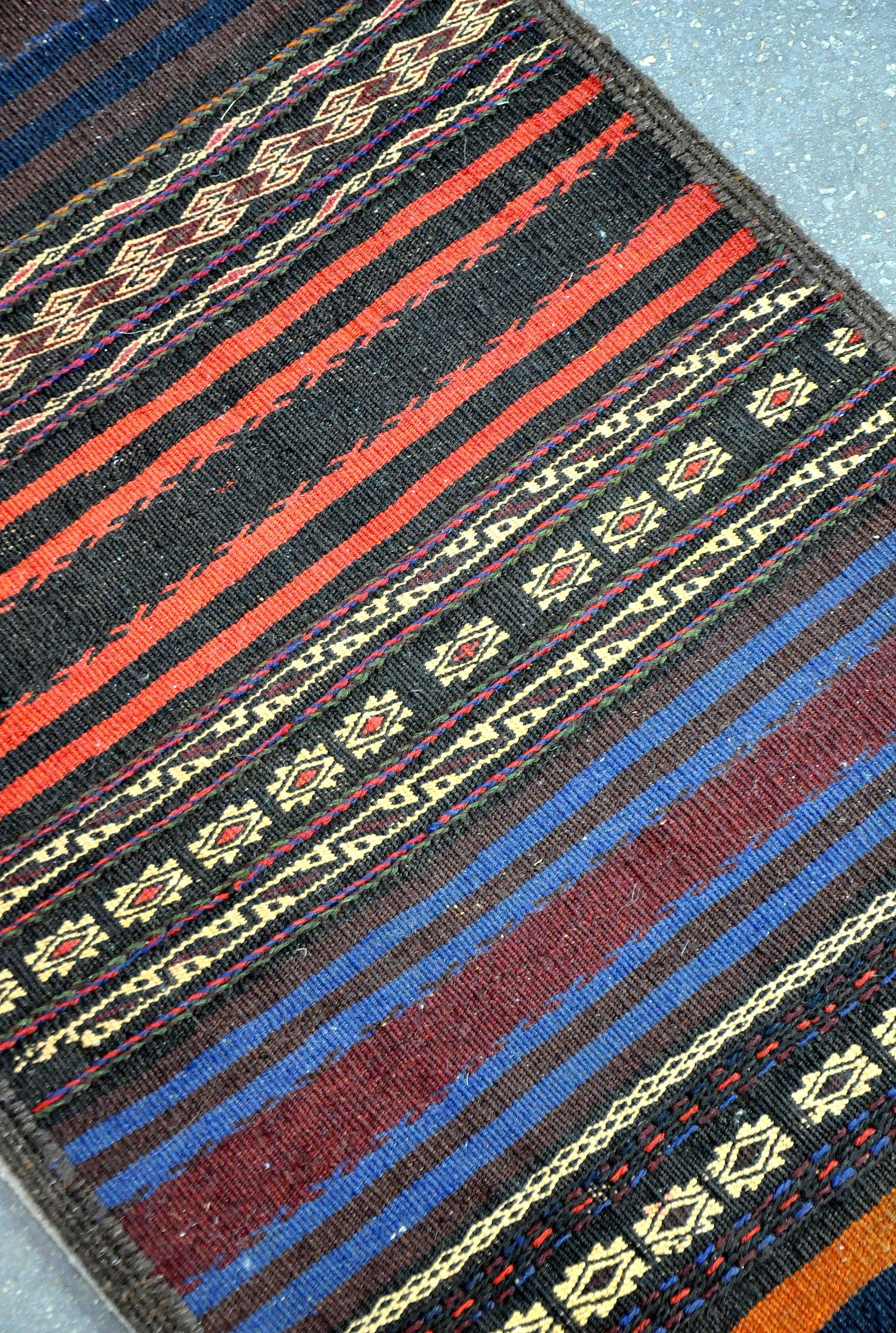 A beautiful vintage handwoven Kilim rug made of vegetable dyed hand spun wool. Vibrant red and blue stripes alternate with geometric designs on a black and brown background. Looks fabulous with Danish or Scandinavian Modern interiors.