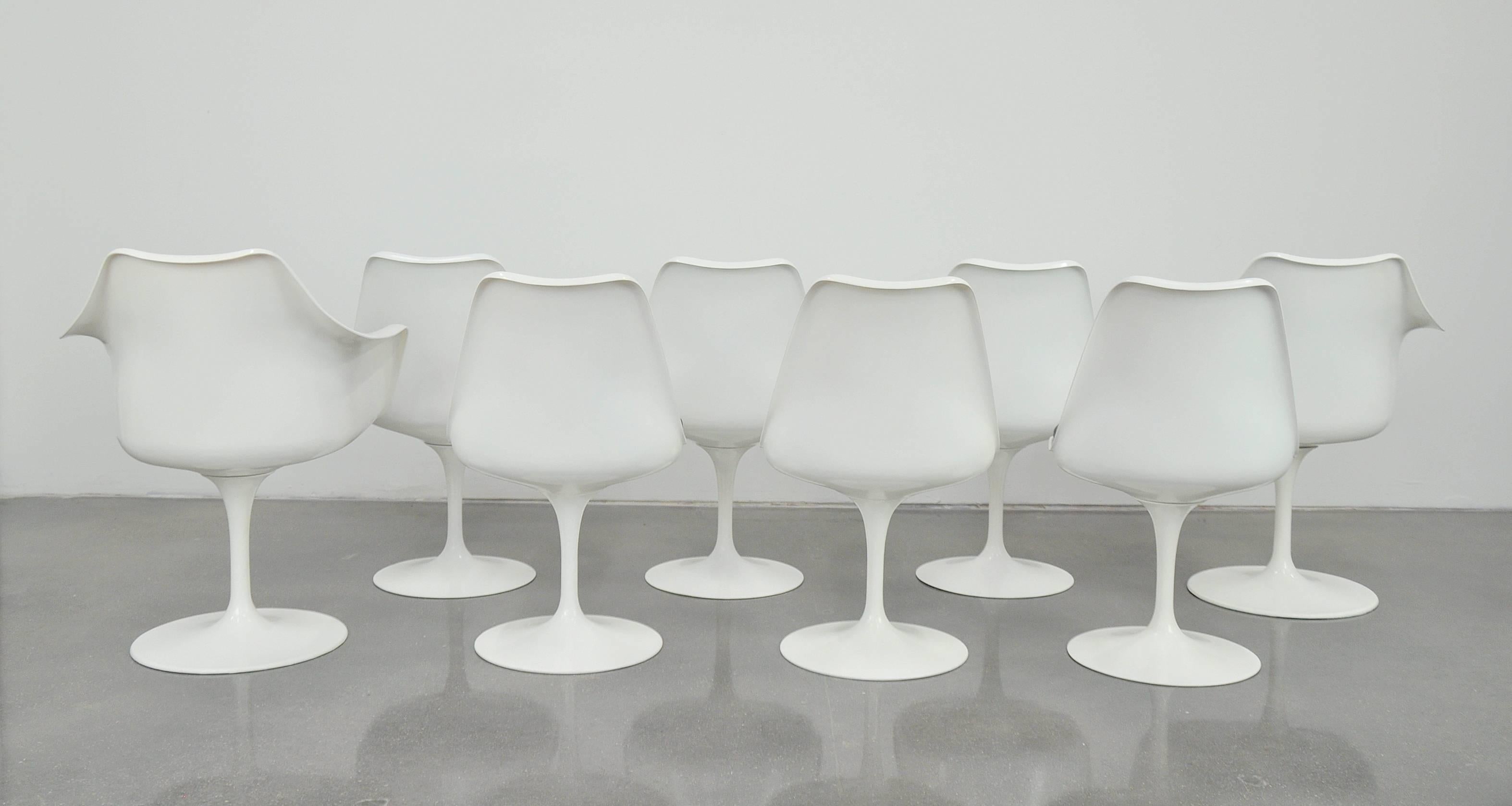 A vintage 1960s set of eight Mid-Century Modern white Tulip dining chairs. All the chairs have new cushions, covered in a period correct, soft, black pebbled faux leather and restored fiberglass shells. The pedestal bases are cast aluminum and have