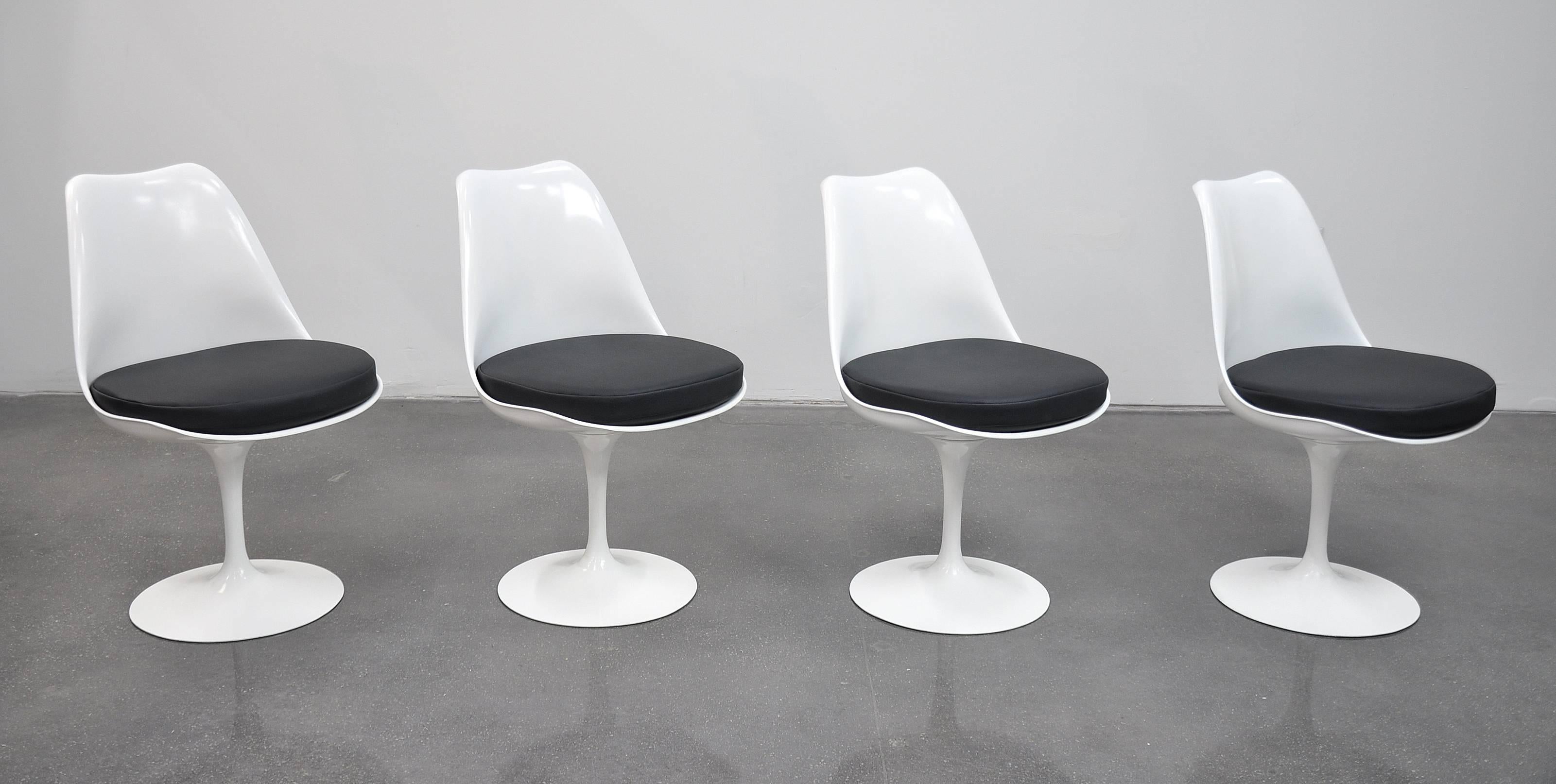 A vintage 1960s set of four Mid-Century Modern white Tulip swiveling dining chairs. All the chairs have new cushions, covered in a period correct, soft, black, pebbled faux leather and restored fiberglass shells. The pedestal bases are cast aluminum