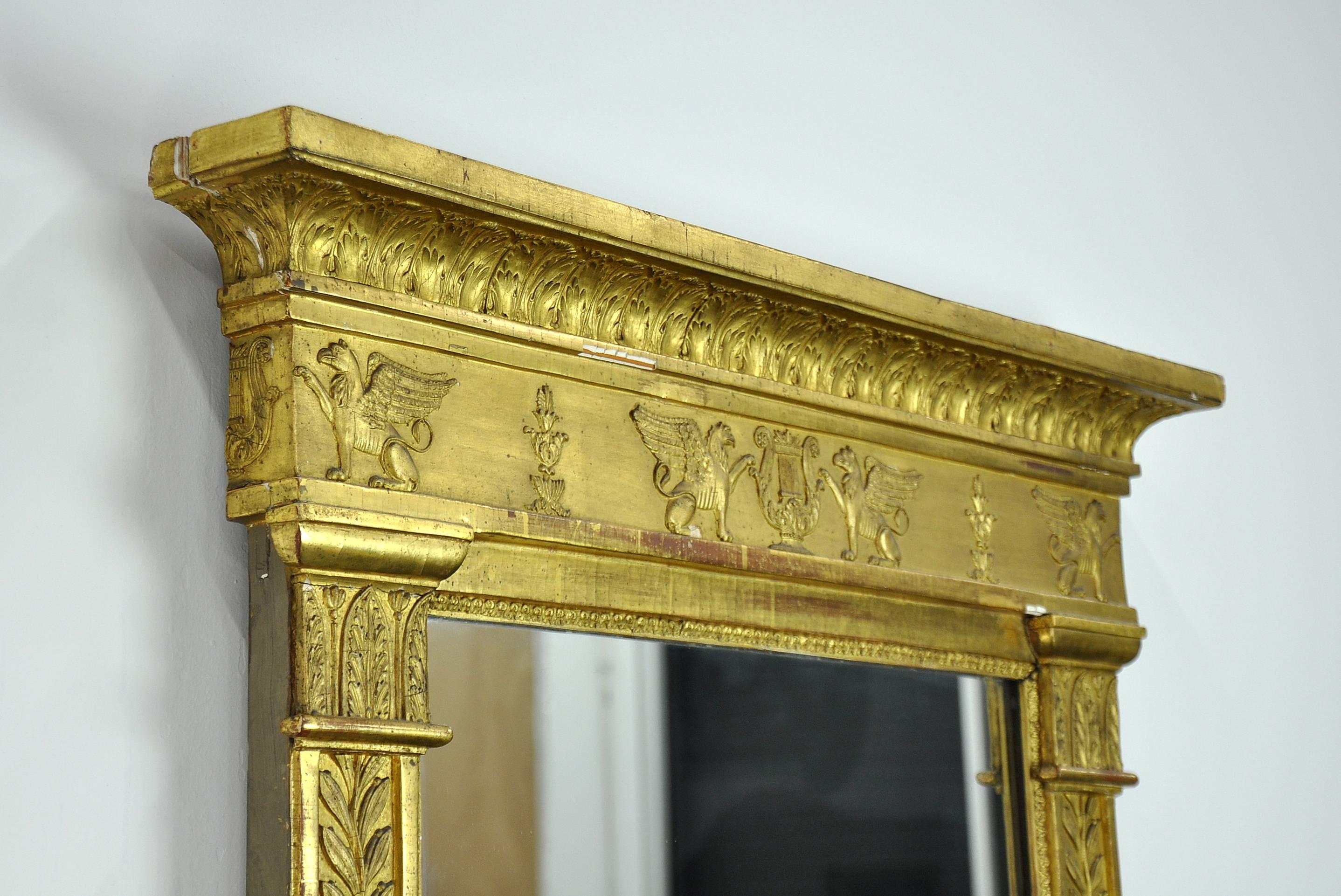 An impressive French First Empire antique gilded trumeau mirror dating from the early 19th century. The giltwood and gessoed wall frame is intricately and abundantly decorated with winged griffins, amphoras, acanthus and olive leaves, lyres and