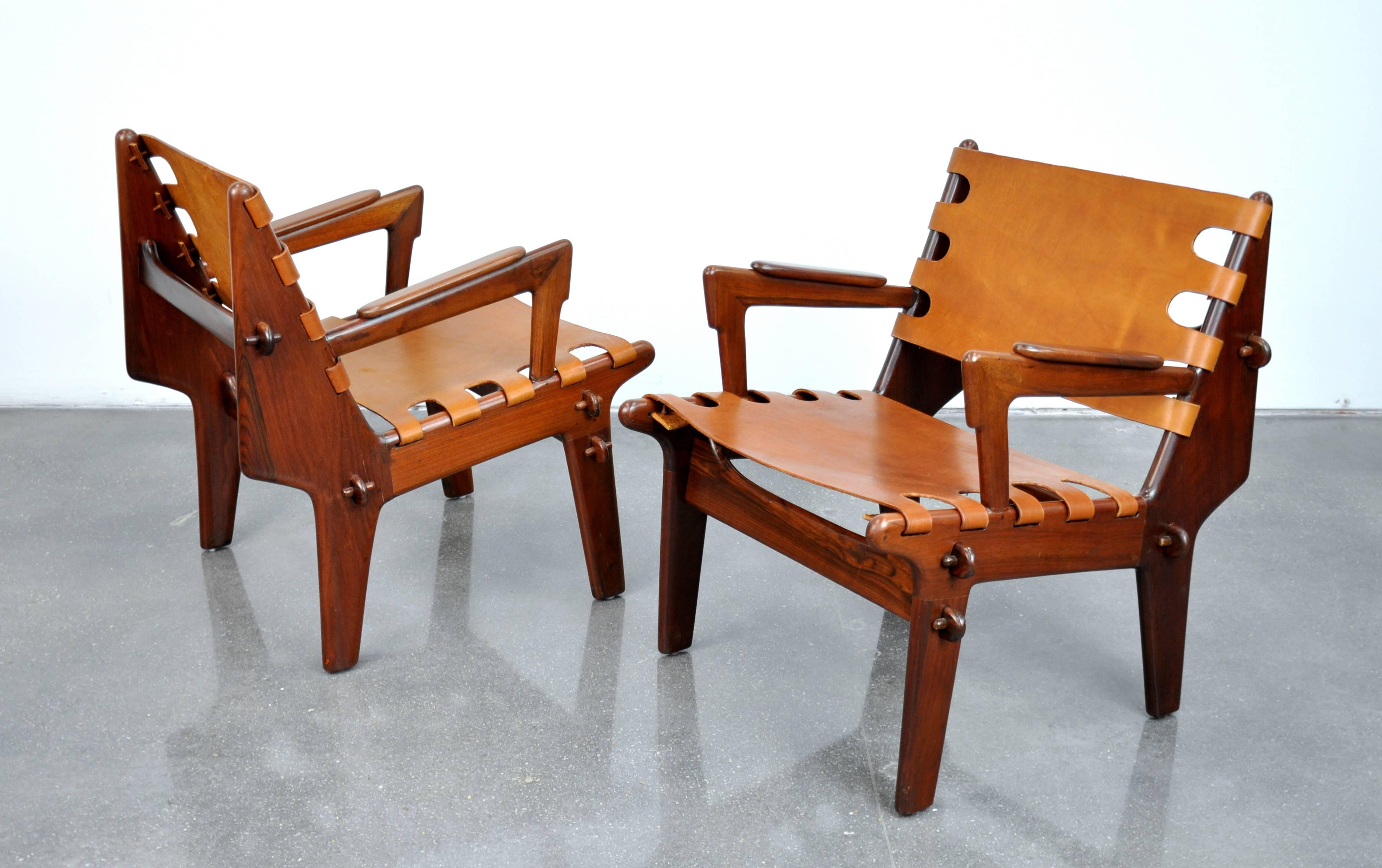 Amazing pair of midcentury Safari style easy lounge chairs and footstool by Ecuadorian designer Angel Pazmino. The sculptural rosewood frames are slung with newer caramel colored leather and feature a wooden peg construction that allows the pieces