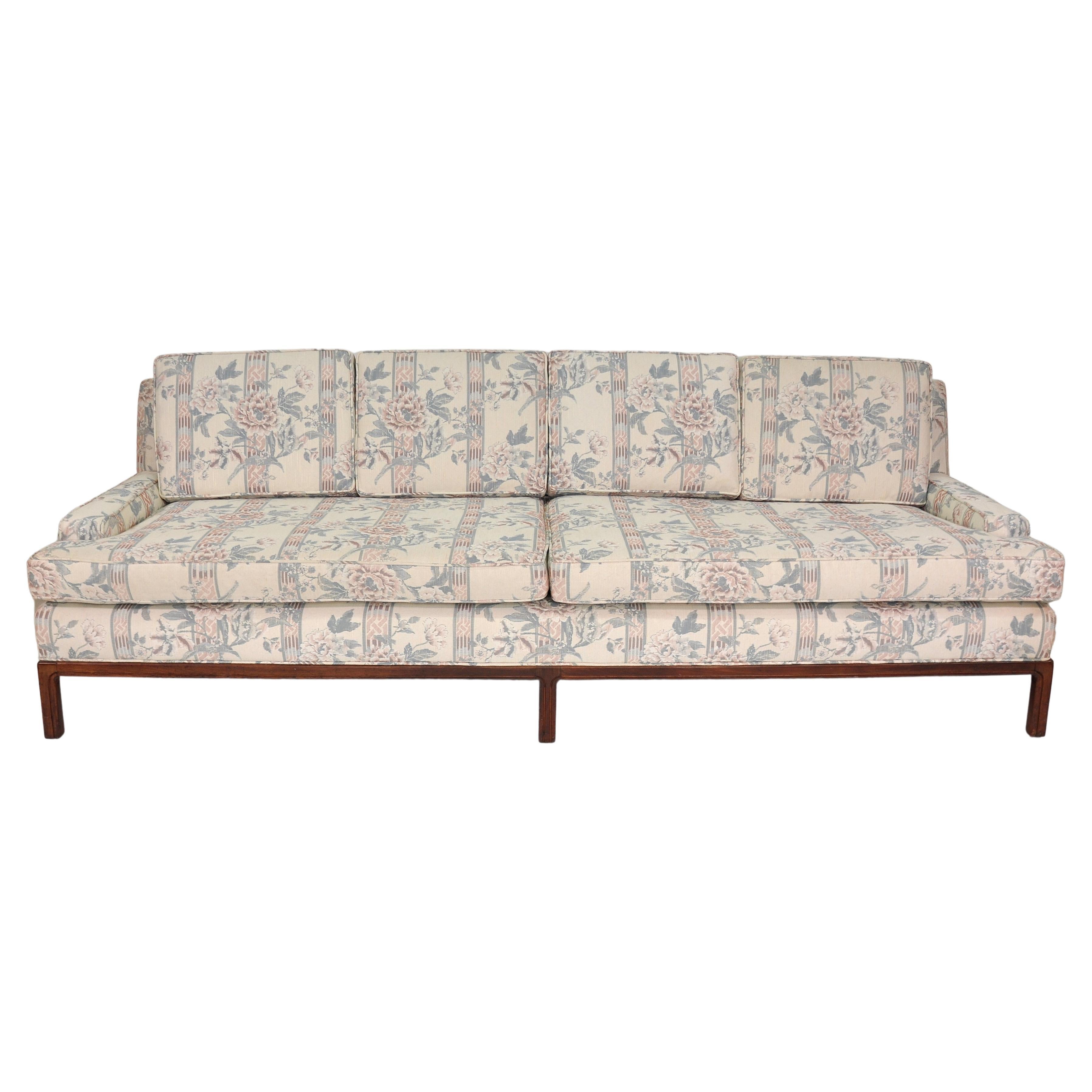 Large four seater vintage sofa in an off-white fabric with light mauve and sky blue accents of geometric stripes and floral patterns with rose motifs. The midcentury couch features a low profile arm style with a slightly inclined seating position