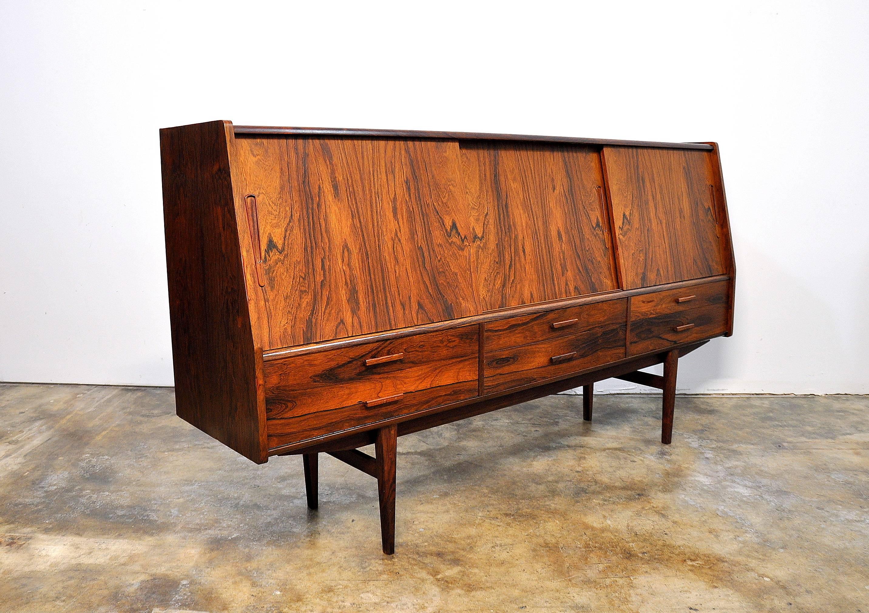 Superb example of a mid-century Danish modern highboard credenza or buffet in Brazilian rosewood featuring a central, mirrored dry bar section with a single shelf and two felt lined drawers, flanked by a pair of cabinet sections with three