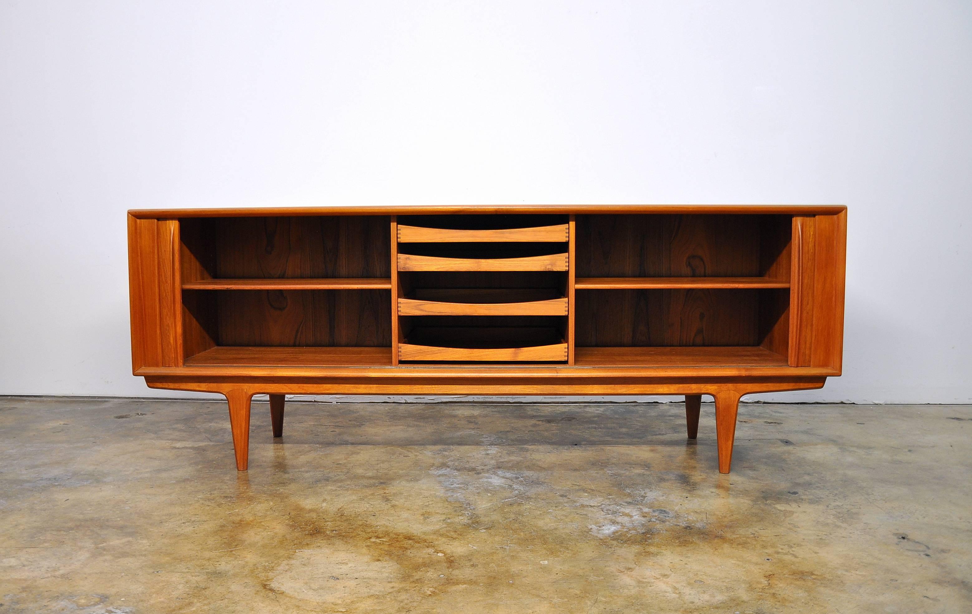 This nearly 7 foot long Mid-Century teak sideboard features two individual sliding tambour doors that allow unobstructed access to the interior. The door fronts have sculpted teak handles and grain patterns that are quite striking. The interior
