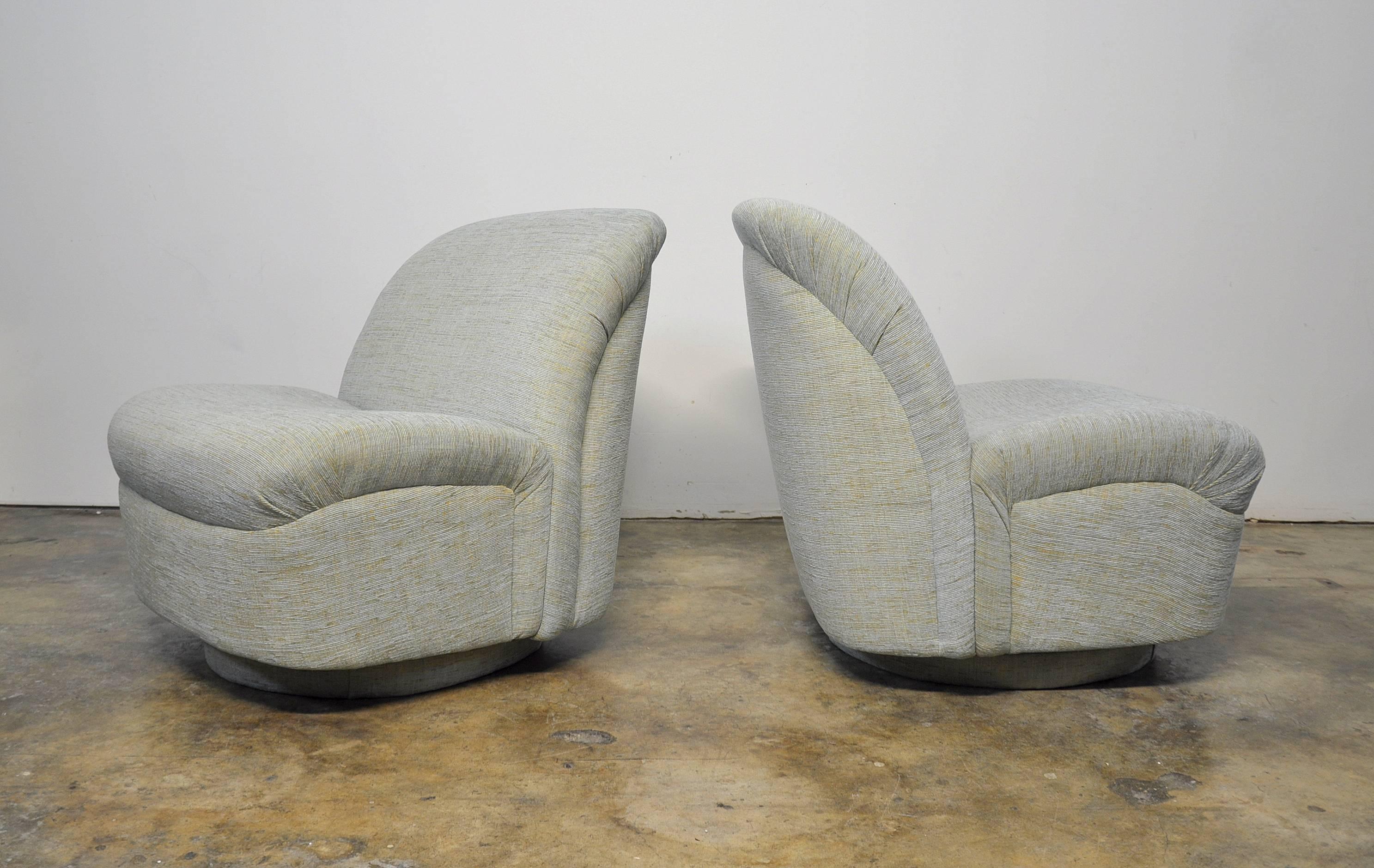 A pair of reupholstered vintage mid-century modern slipper chairs available. They swivel, tilt, rock and are extremely comfortable. Each chair has been recovered in a light blue and yellow chenille. The clam shape design of these chairs is