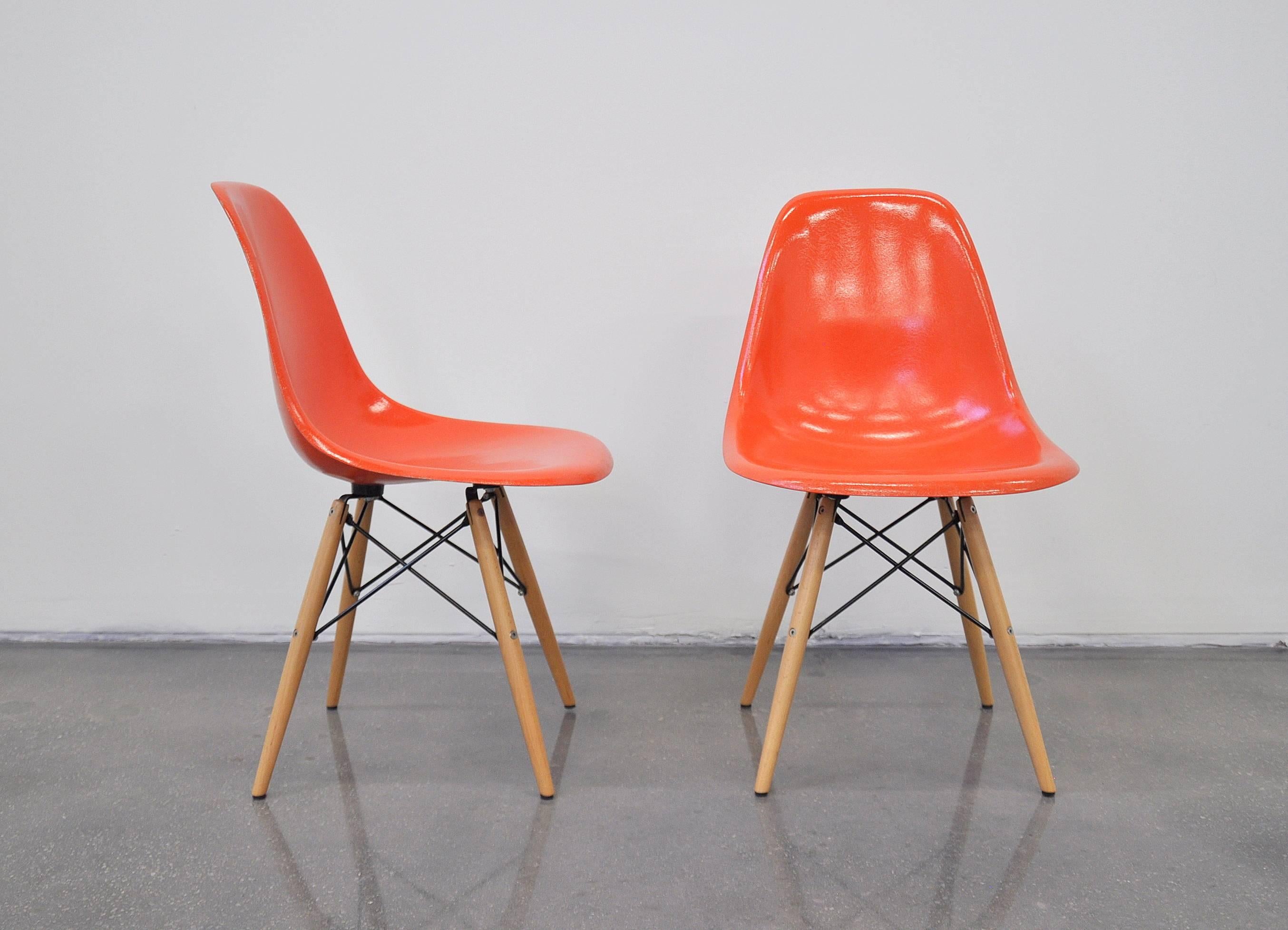 A vintage pair of Mid-Century Modern DFSW shell chairs designed by Charles and Ray Eames for Herman Miller available, dating from the late 1950s. The pair of dining or side chairs feature orange fiberglass shells and maple wood dowel legs. Works