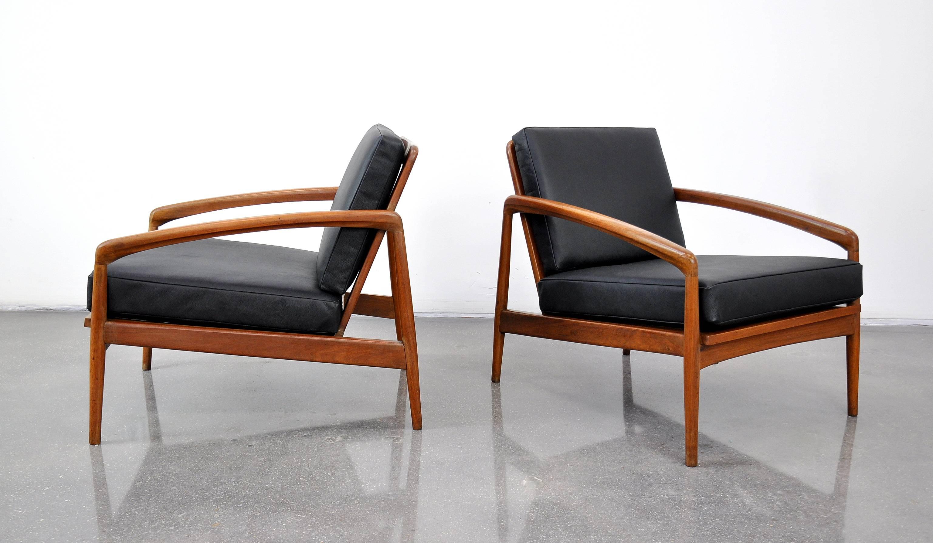 A pair of vintage Mid-Century teak easy chairs, dating from the 1950s and attributed to or in the style of designer Kai Kristiansen's Paper Knife chairs. The frames have sleek, slender arms, slatted backs and seats, and new removable cushions in