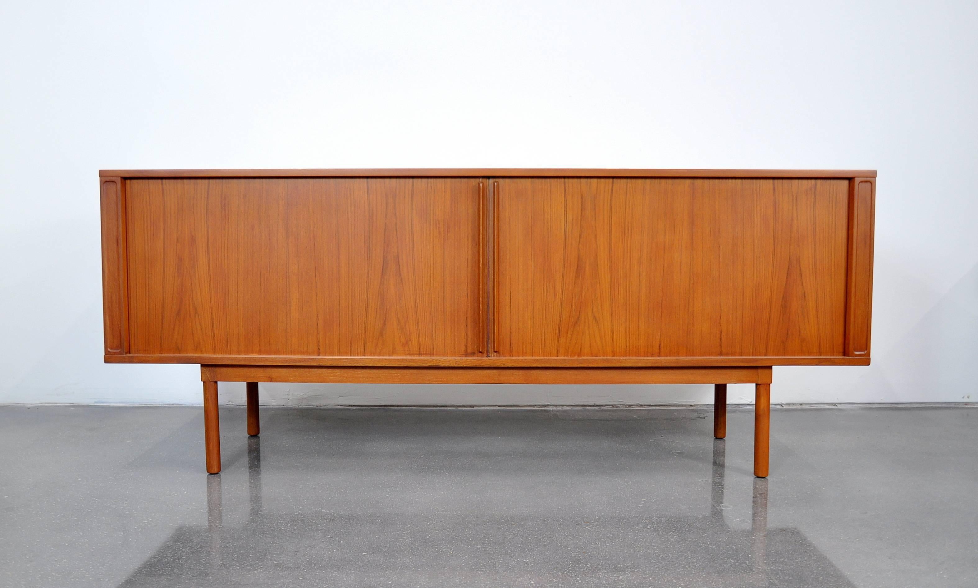 Beautiful Mid-Century Danish modern teak credenza or bar cabinet designed by Jens Quistgaard for Lovig; made in Denmark, circa 1971. The sideboard features two large tambour doors allowing unobstructed access to the interior. Each door is