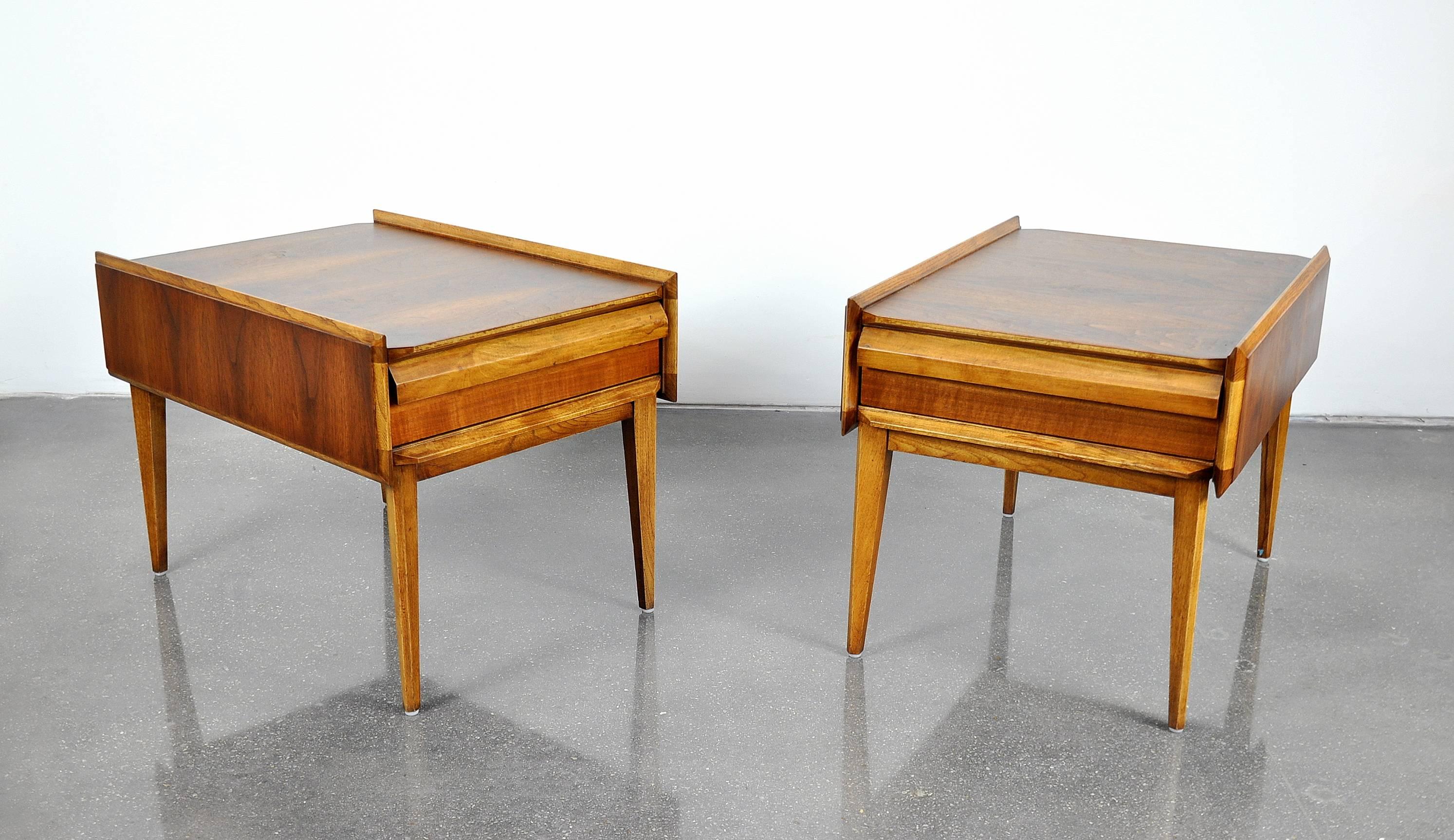 A great pair of Mid-Century Modern end tables from the very hard to find First Edition collection manufactured by Lane Furniture, Altavista in the 1950s. The walnut and pecan occasional tables feature a drawer with a sculpted louvered integrated