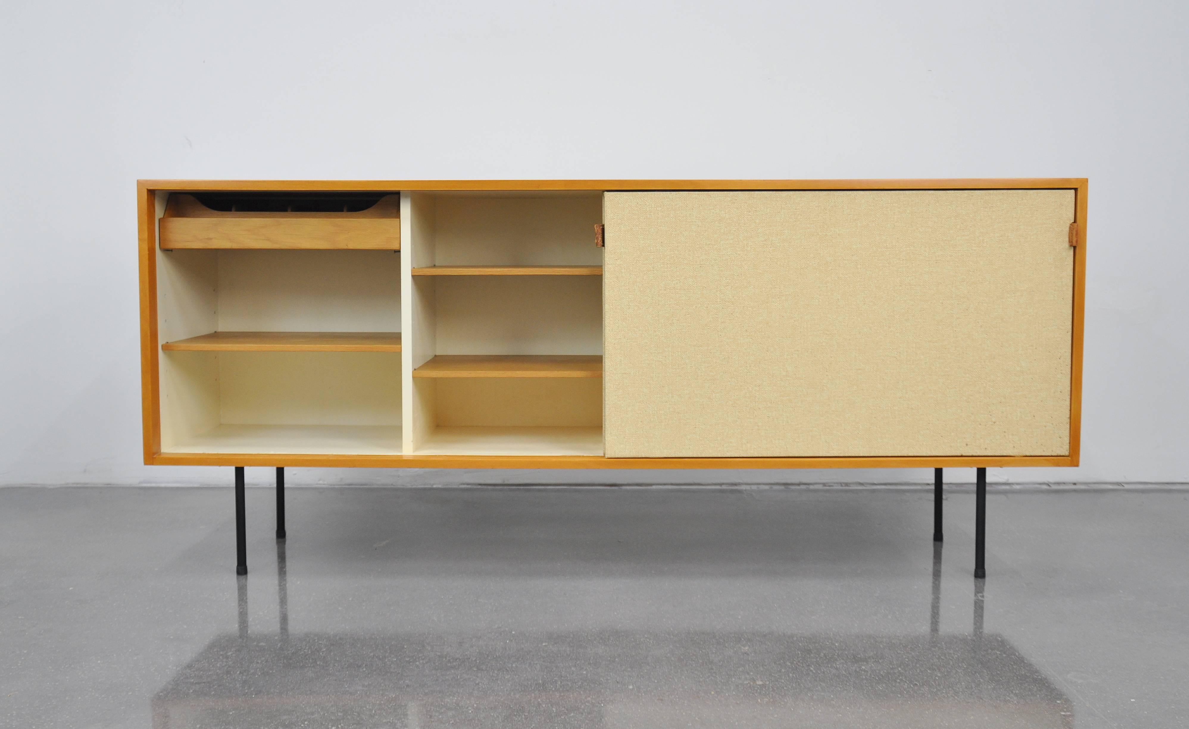 A superb model 116 Mid-Century Modern cabinet designed by Florence Knoll for Knoll Associates in 1948. The vintage sideboard or bar features a pair of sliding doors with seagrass fronts and saddle leather handles, opening to a white lacquered