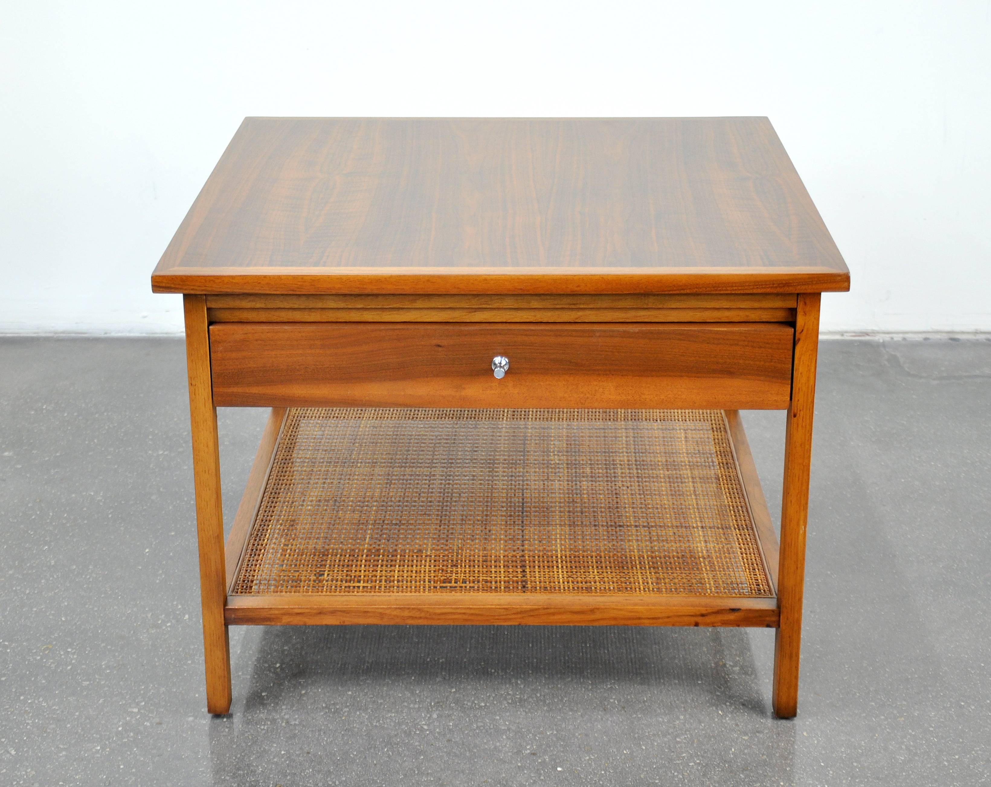 A Mid-Century Modern end or lamp table designed by Paul McCobb for the Lane Delineator series, only produced between 1961 and 1965. It features a single drawer with signature pull and a caned magazine shelf. Having a finished back, it could also be