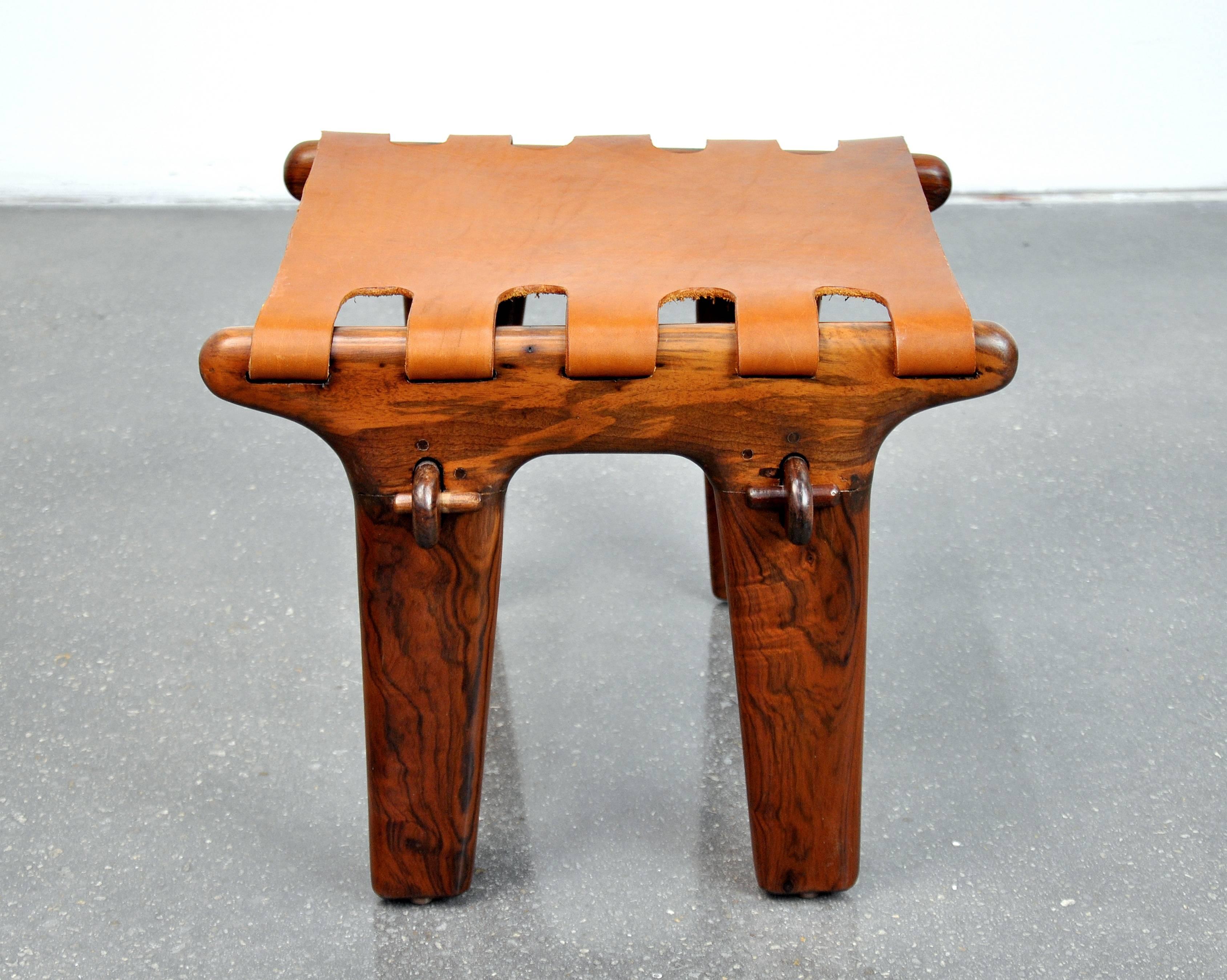 Amazing midcentury safari style footstool by Ecuadorian designer Angel Pazmino. The sculptural rosewood frame is slung with newer caramel colored leather and features a wooden peg construction that allows it to be taken apart for easy transport. In