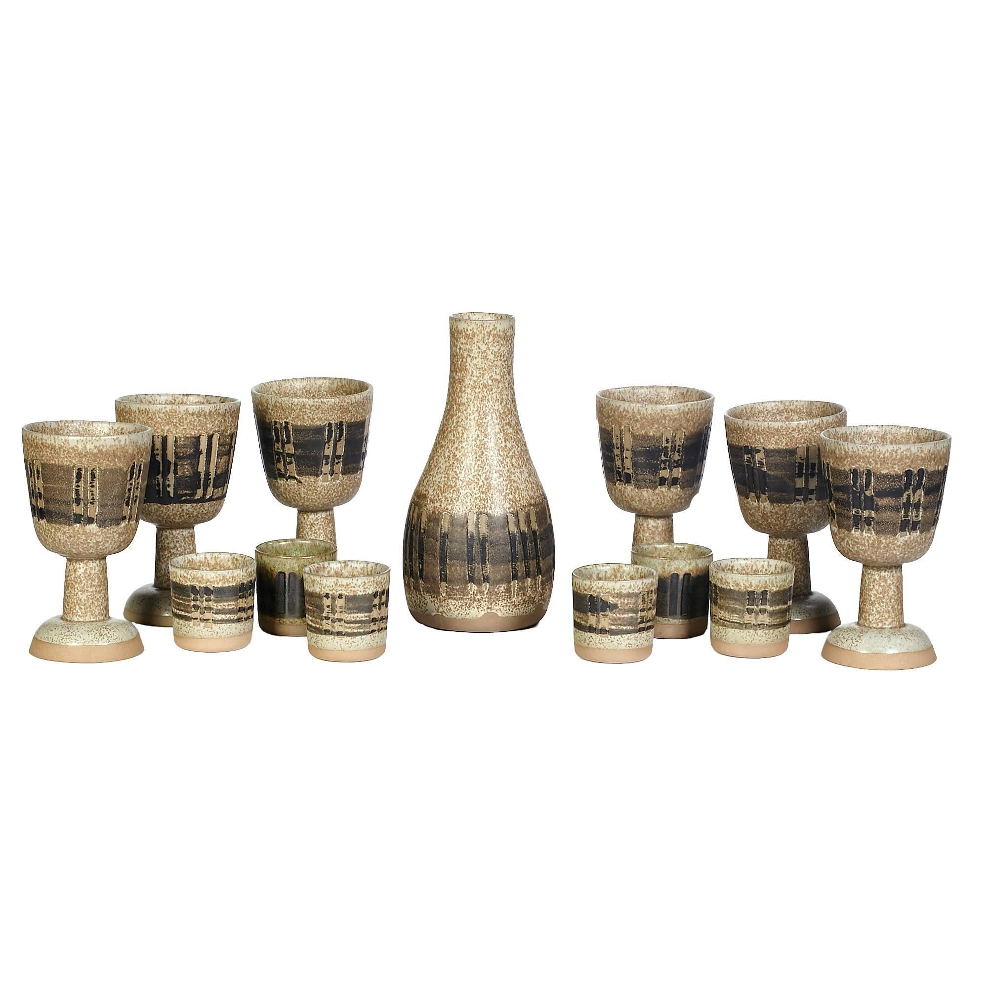 Gordon and Jane Martz for Marshall Studios 1960, 13-piece handmade ceramic beverage set with six footed tumblers, six small tumblers and a carafe. The set has a speckled background with a various brown stripe design. The footed tumblers are 3.75