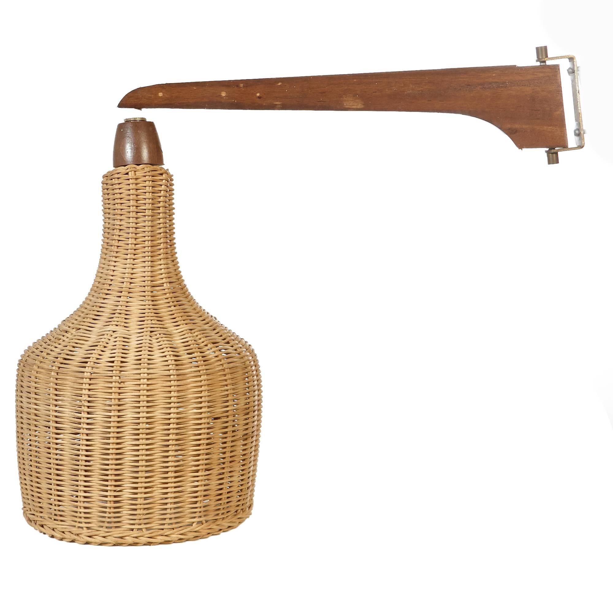 A large wall-mounted lamp with a wicker shade on an adjustable swing wooden arm. Plug is wired for the US and in working condition. Unmarked. One very small break in the wicker, not seen.