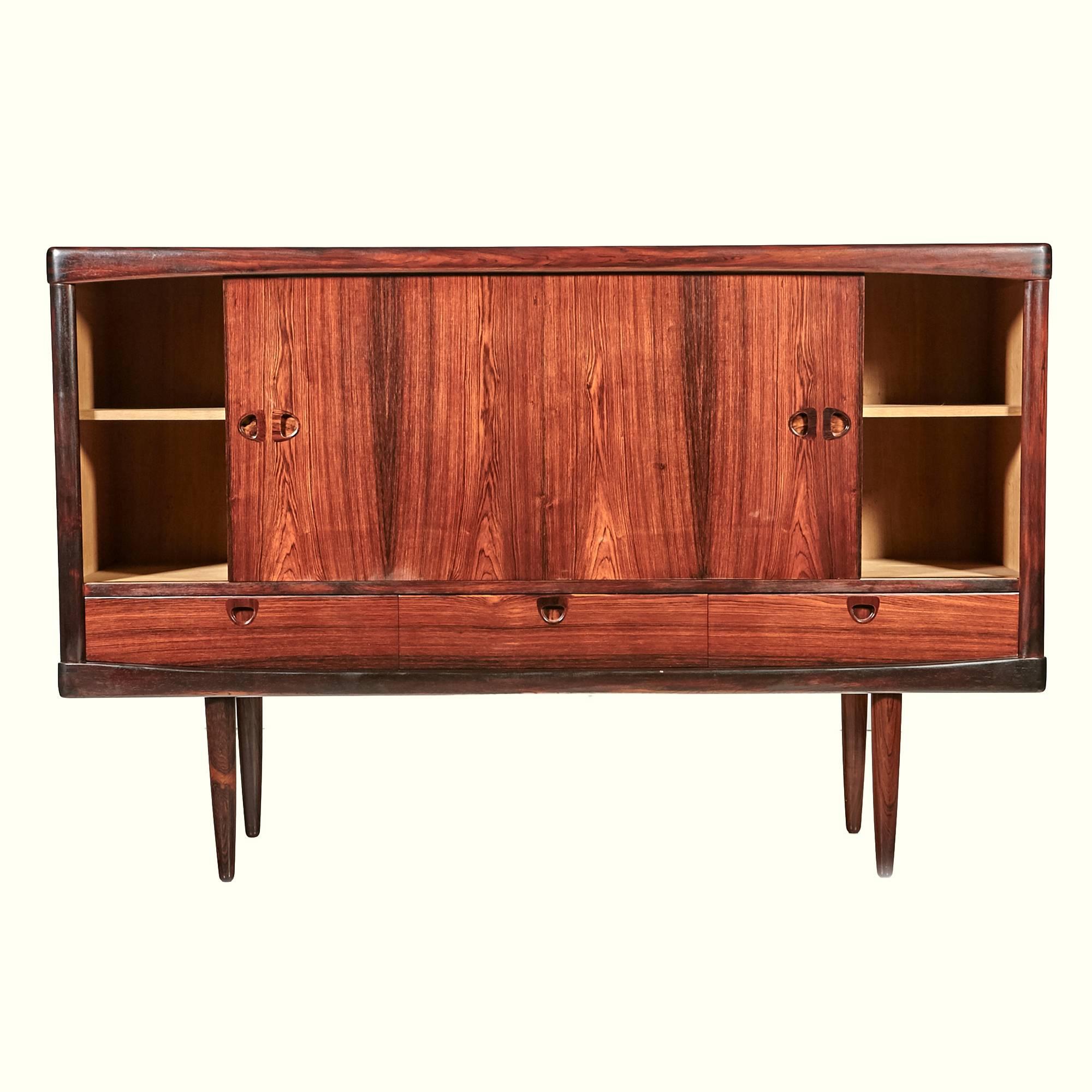 Danish rosewood sideboard credenza designed by H.W. Klein for Bramin of Denmark. The sideboard has sliding front doors with shelving storage behind them and three additional drawers. Finished rosewood backing and exposed dovetail accents.