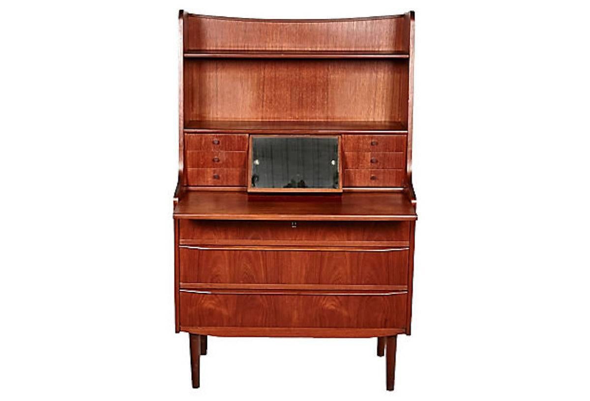 1960s Danish teak secretary desk that also serves as a vanity. The desk pulls out for writing and has a mirror built-in. The desk has six small drawers and open shelving for storage. There is three full-size larger drawers for additional storage.