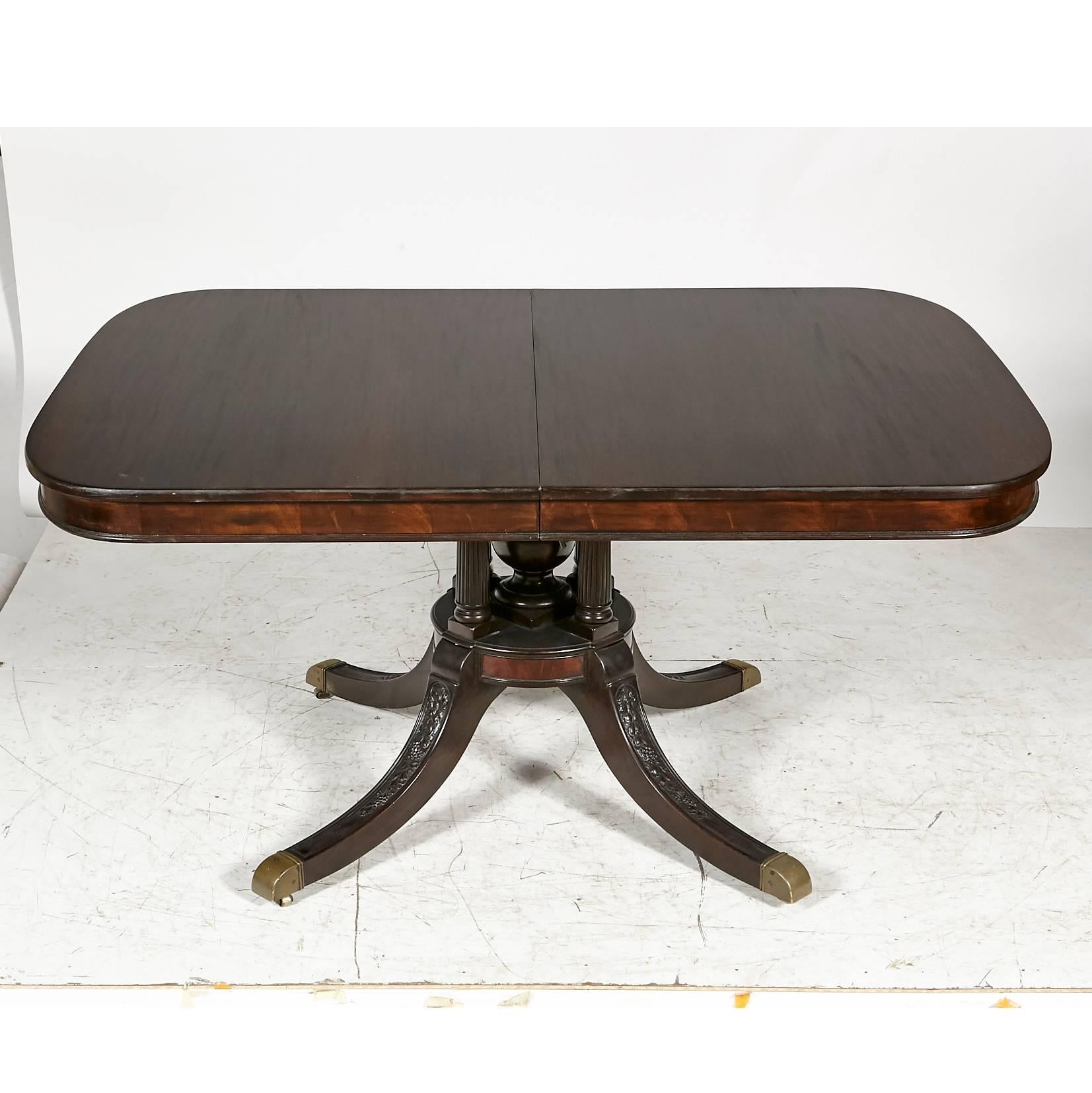 Regency-style mahogany wood banquet dining room table with five additional boards. The base has four columns and hand-carved fruit all accented with brass feet. When the table is fully open there are four legs that pull down to support the table