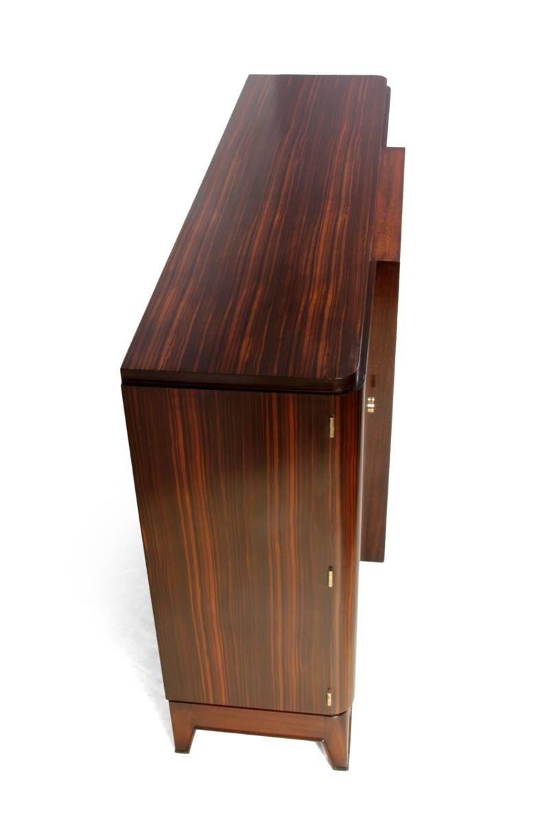 French Art Deco sideboard in Macassar ebony, circa 1930

This Art Deco sideboard was produced in France in the 1930s it has three doors the central door being glazed with brass surround and glass shelves behind, the door to the left is sycamore