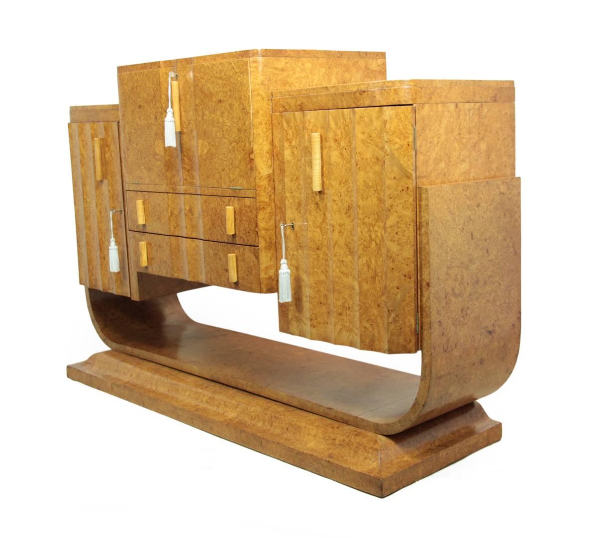 Art Deco walnut cocktail sideboard.
Sitting on a U-shaped base this Epstein brothers' sideboard was constructed in 1930s in London. It has fluted cupboards to the left and right and a pop up cocktail bar in the center, with two drawers below this