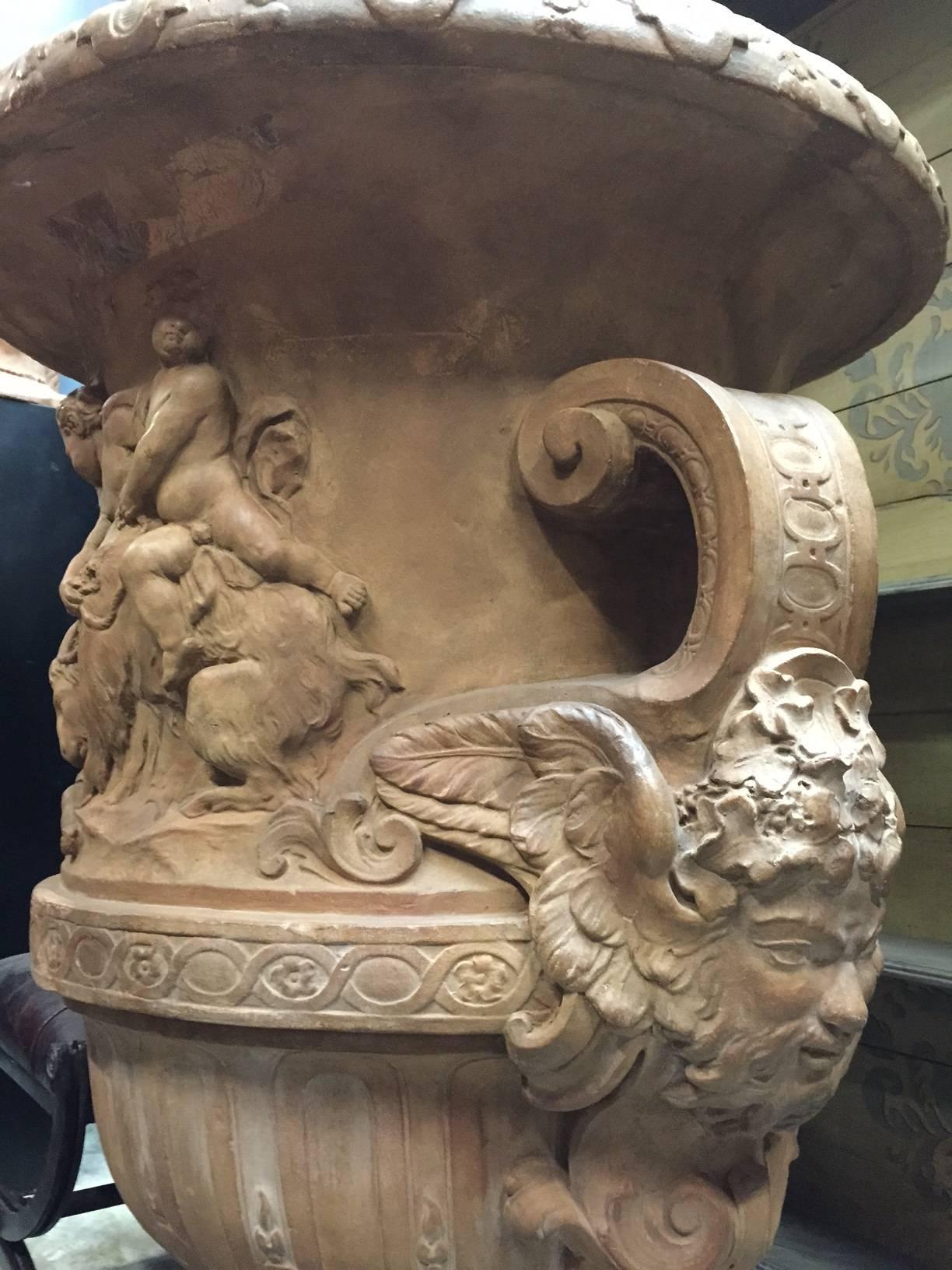 This monumental Italian neoclassical style terracotta Campana-form garden urn with masked handles. An extremely fine molded figural group of children in play all around the urn.
Being exposed to the outdoor elements has caused a beautiful patina,