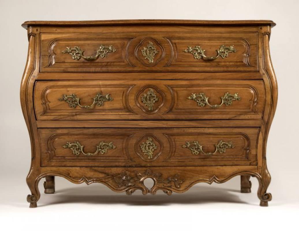 A French 18th century Louis XV Provincial finely carved walnut commode. The serpentine fronted commode with three long carved bombe drawers with bronze handles, all supported by scrolling cabriole feet.