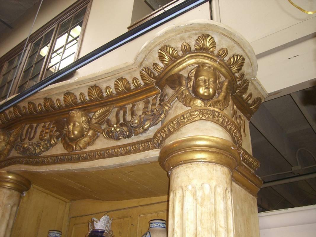 Magnificent 19th century Italian monumental finely carved, painted and parcel-gilt architectural bookcase topped with leaf-motif crown above pediment with five putti, each flanked with wings, conjoined with floral garlands and ribbons over three