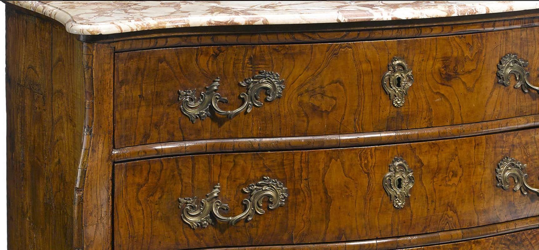 Imposing 18th century Italian Rococo elmwood commode topped with a white and brown mottled serpentine fronted marble top over three-drawer commode veneered with exotic elmwood mounted with original intricate foliage bronze handles supported by