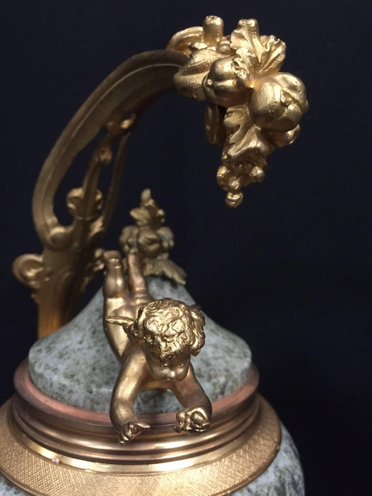 Lovely pair of unusual French ormolu-mounted green marble urns with cherubs. Ormolu foliage with fruit and scrolls over mounted finial and flying cherub on spotted green marble on square marble base.

The measurement of the base is 4