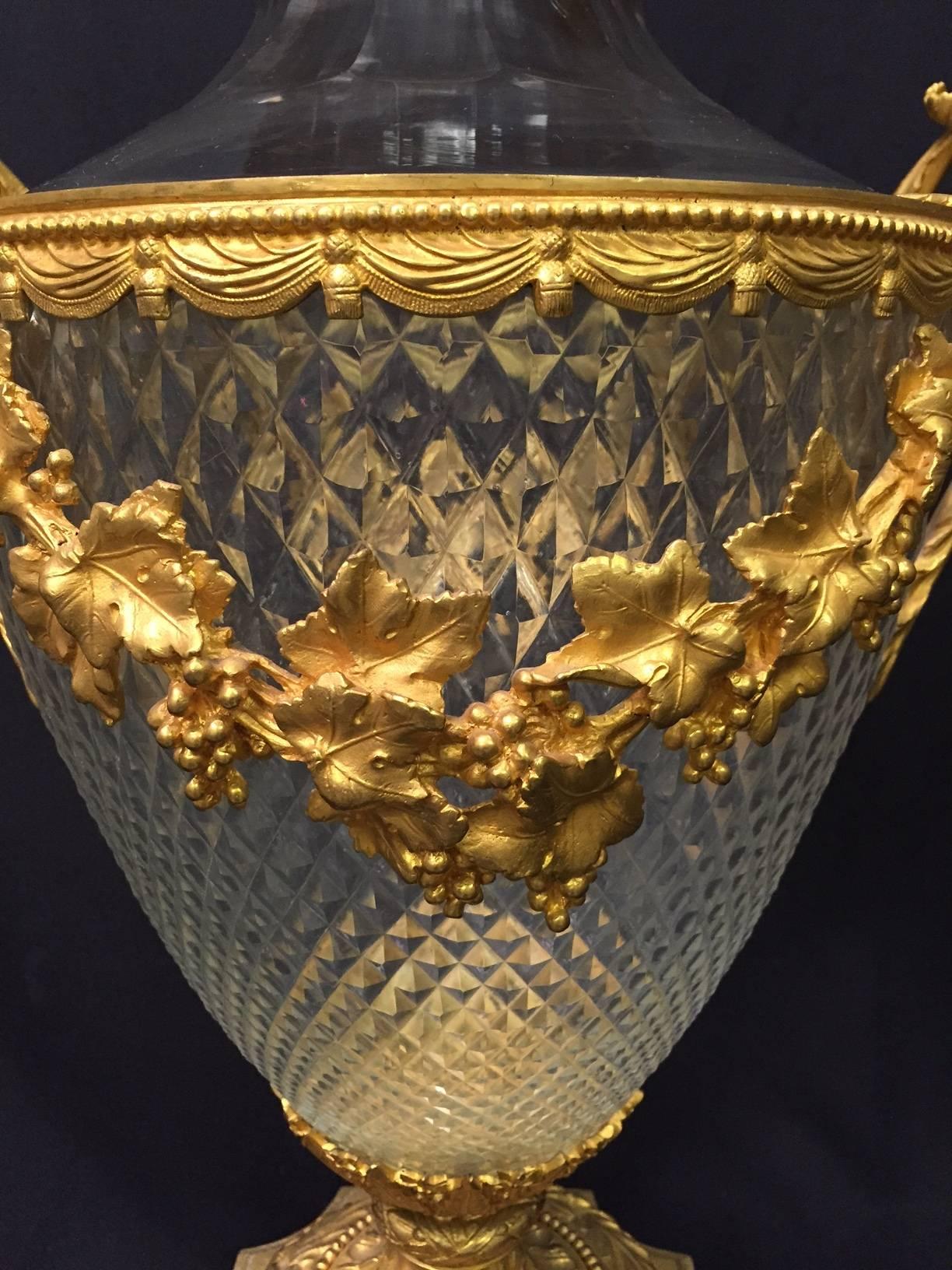 Large remarkable French ormolu-mounted and cut crystal covered urn. Topped with ormolu cover and large fruited finial on cut crystal urn mounted with fruit and leaf swags and handles, on fluted base inset in a wreath over a plinth.

The