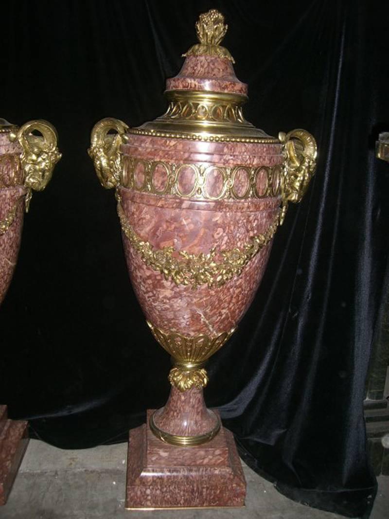 Very large pair of French Louis XVI style ormolu-mounted
rouge marble covered urns with ram's head handles, circa 1900. Marble covers are topped by fruit and floral finial over large ormolu-mounted ovoid body with an intricate floral swag and