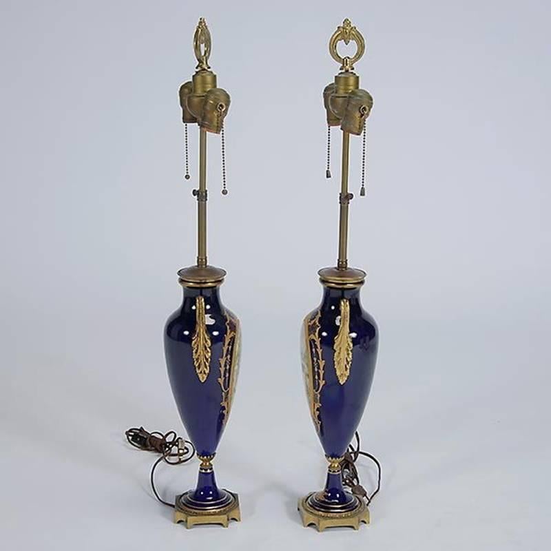 Elegant pair of French Sèvres style porcelain urns mounted lamps, first half of the 20th century.
Each vase with oval hand-painted signed romantic scene of French man and woman surrounded by beautiful gold tracing with scrolling acanthus bronze