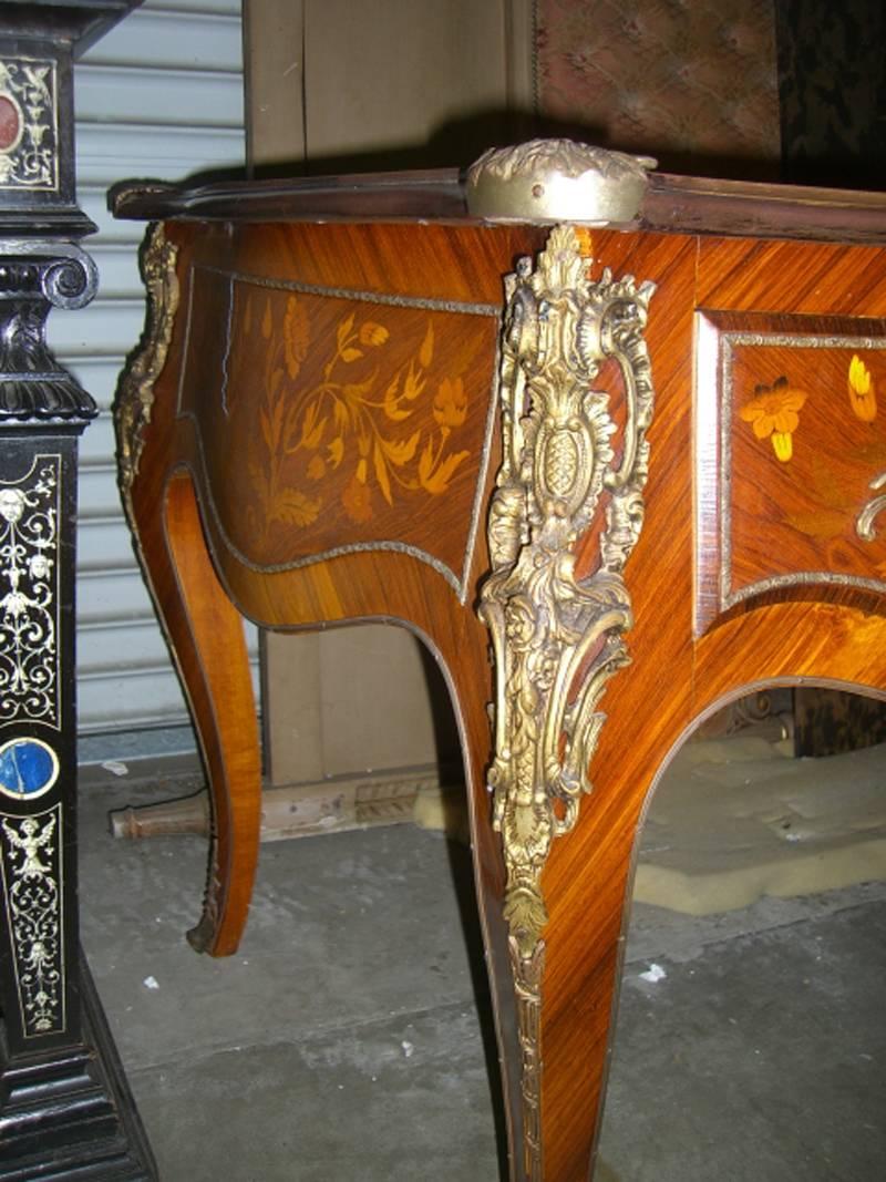 French Louis XV style bronze-mounted marquetry kingwood bureau plat desk, 19th century.

The beige and gold trimmed leather top over three curved drawers with floral marquetry inlay and bronze mounts throughout all sides of the frieze, on four