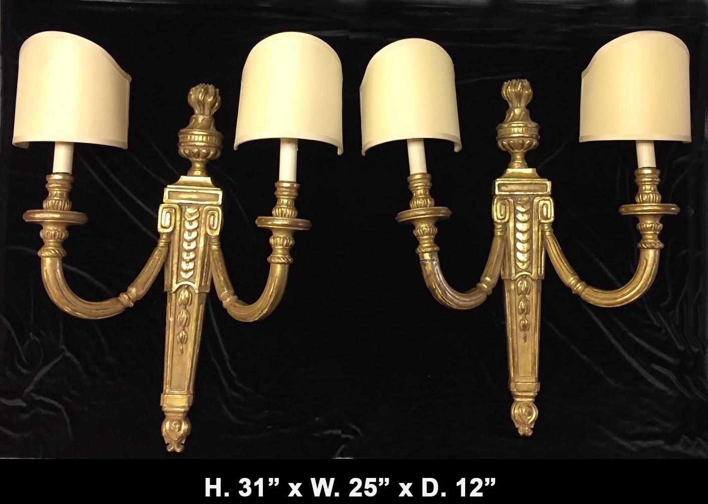 Pair of large Italian neoclassical style 22-karat gold leafed carved wood two-light sconces with flamed urn finials and large curved silk shades.

Overall Dimensions are listed below include the shades.