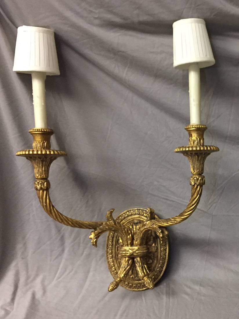 Pair of large Louis XV style 22-karat gold leafed carved giltwood two-light sconces with finely carved oval medallion back plate and pleated fabric shades, late 20th century.

Distressed finish.

 