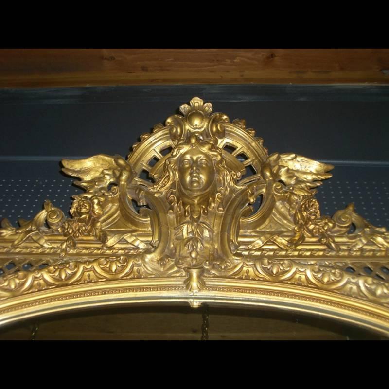 Monumental 19th century French Louis XVI style giltwood and gesso mirror. The arched plate below an elaborate cresting of pierced work and scrolling ornaments with a beautifully carved female mask within a central decorated pediment flanked by angel