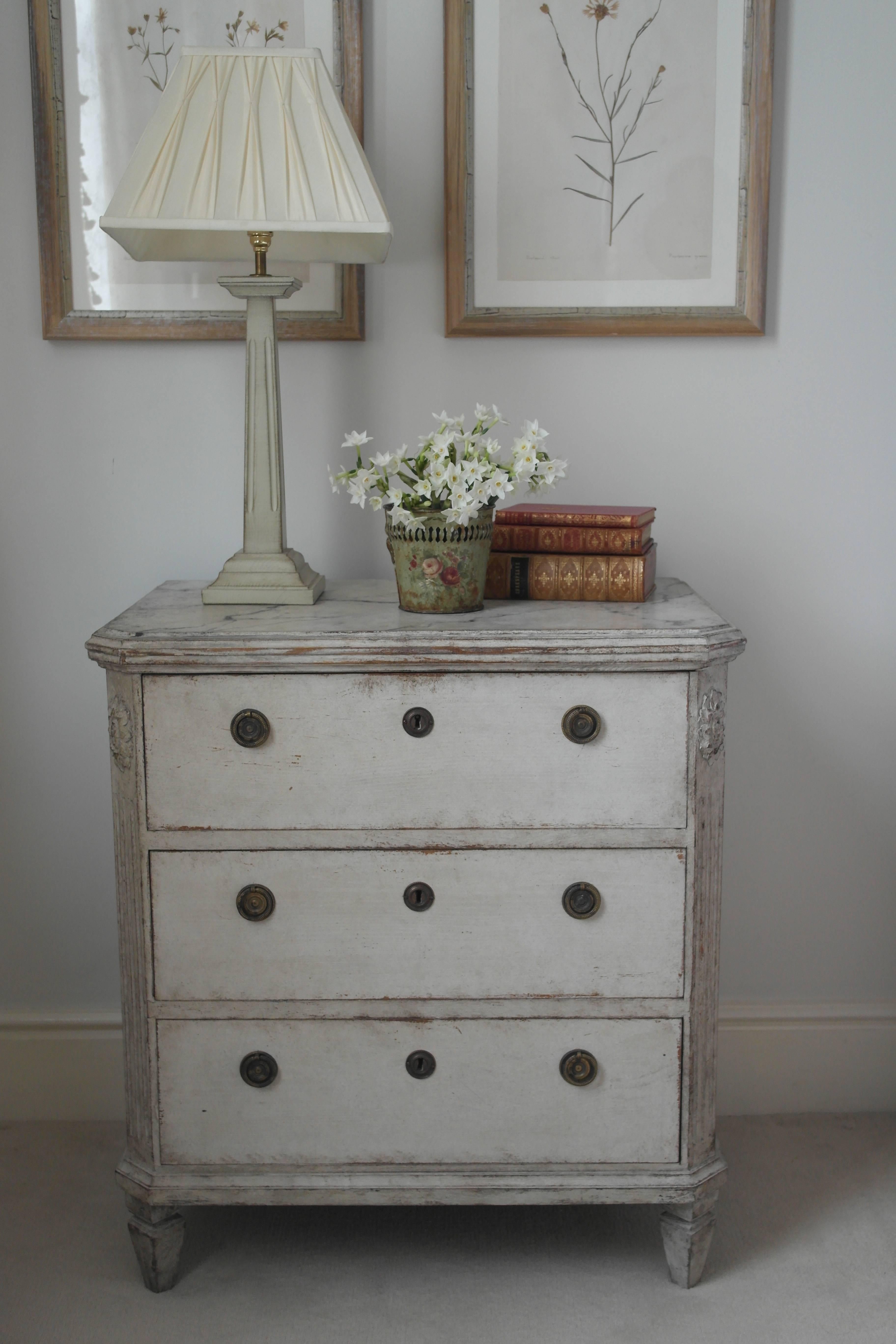 A pair of three-drawer painted Swedish commodes in the Gustavian style featuring hand-painted faux marbled tops, canted corners and feet and simple hardware. Useful small size - ideal to use as bedside tables.